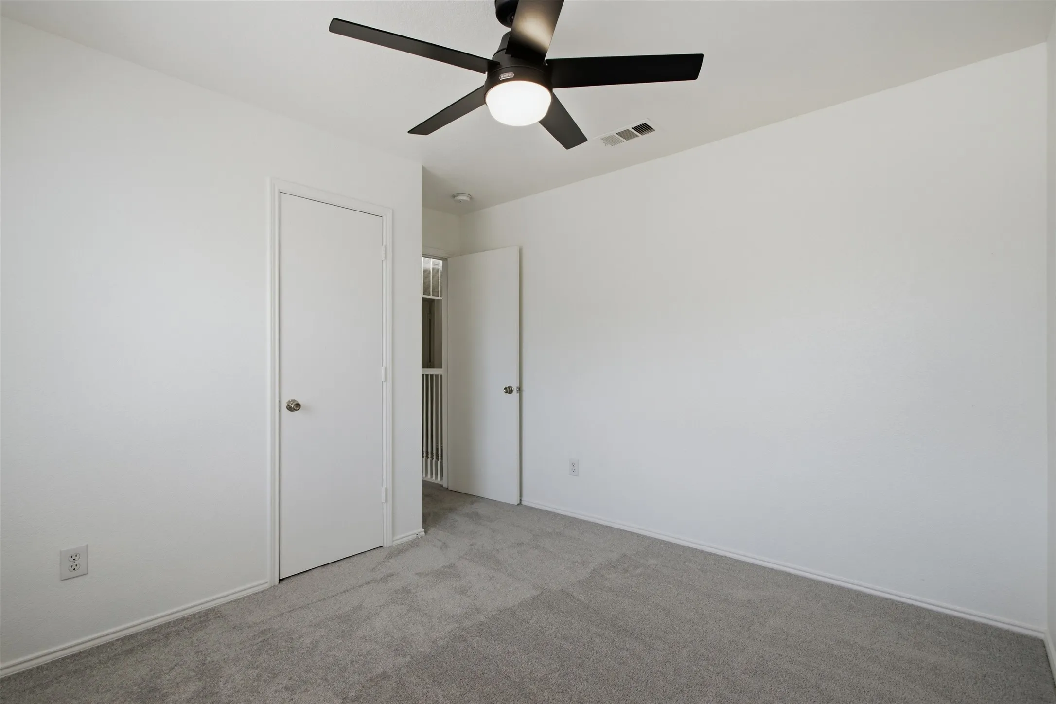 Carpeted room featuring a matte black ceiling fan with integrated lighting, white walls, white trim, and a white interior door with a brushed nickel knob