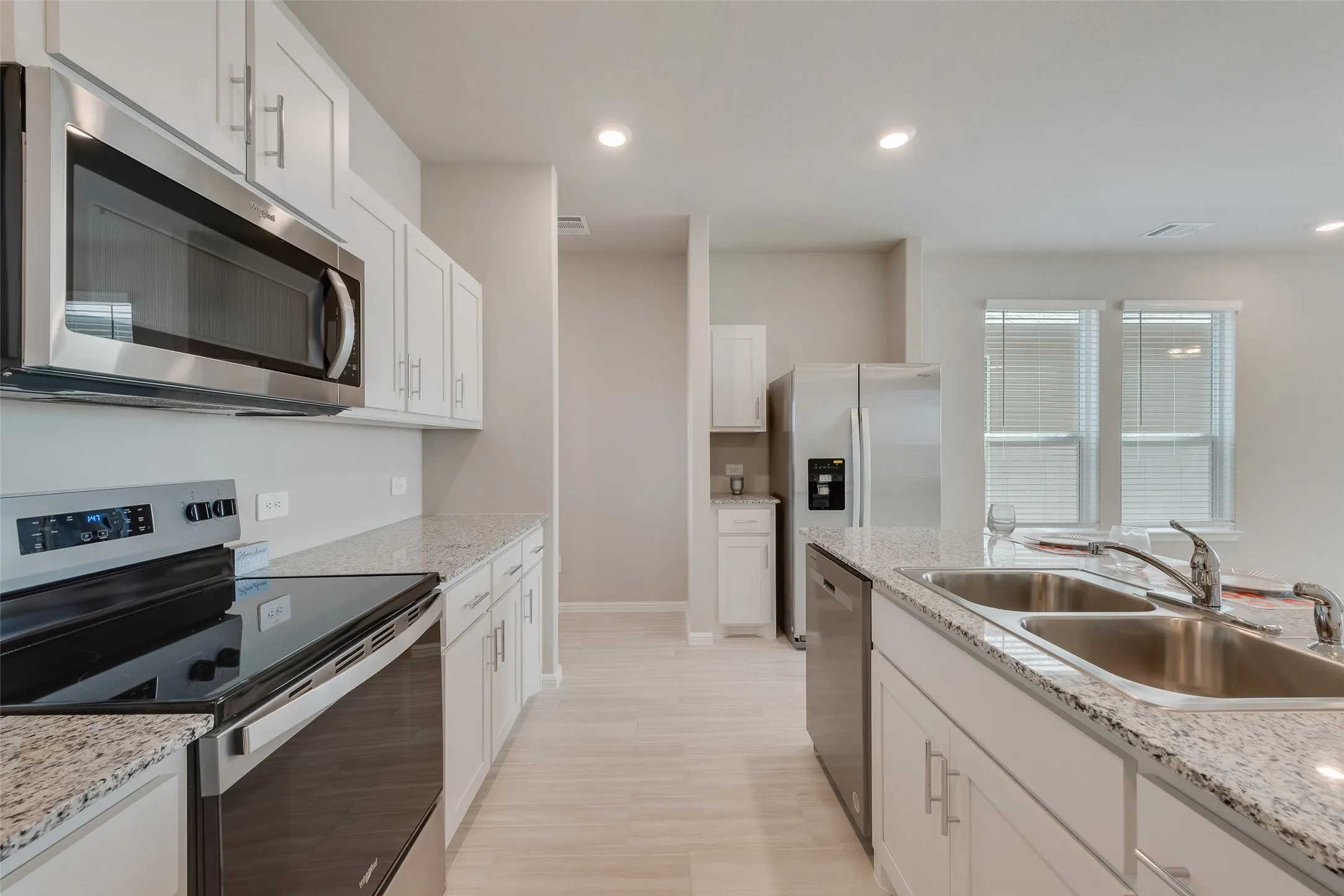 Kitchen featuring stainless steel appliances, white cabinetry, granite countertops, and wood-finish flooring