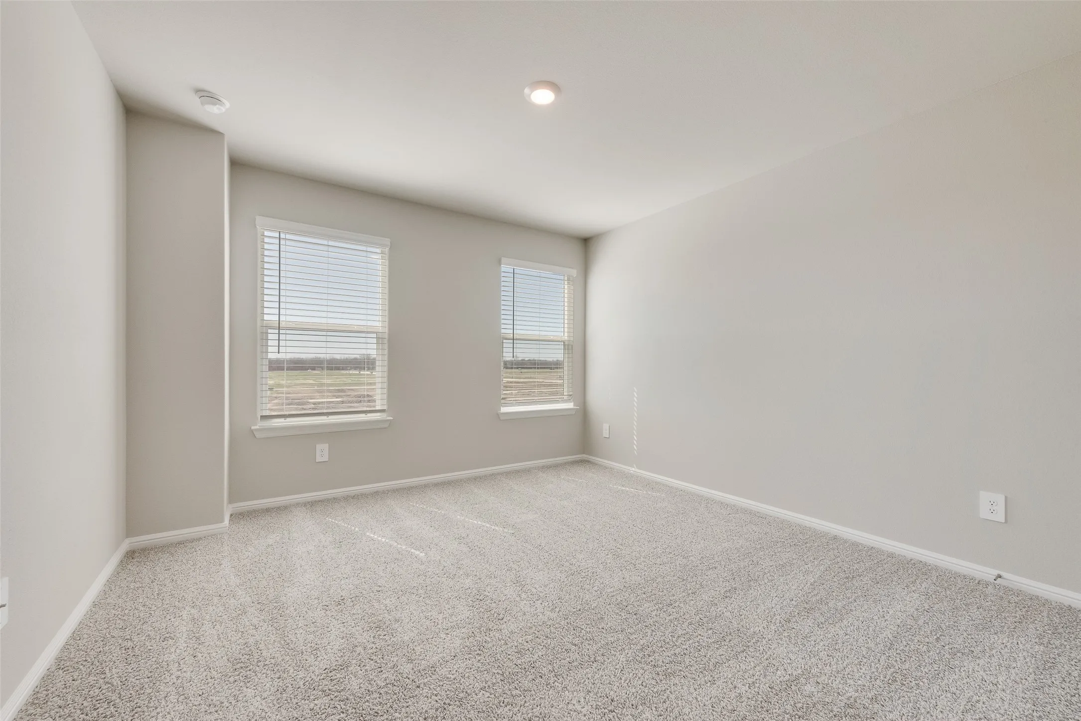 Neutral paint palette, recessed lighting, two windows with blinds, and light-colored carpeting