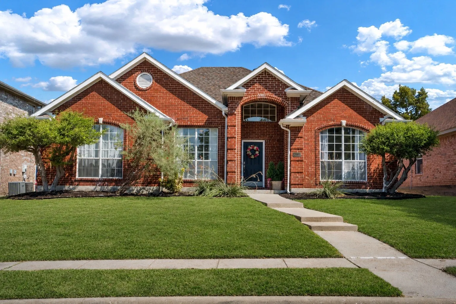 Red brick facade with arched windows, a dark entry door, and a concrete walk