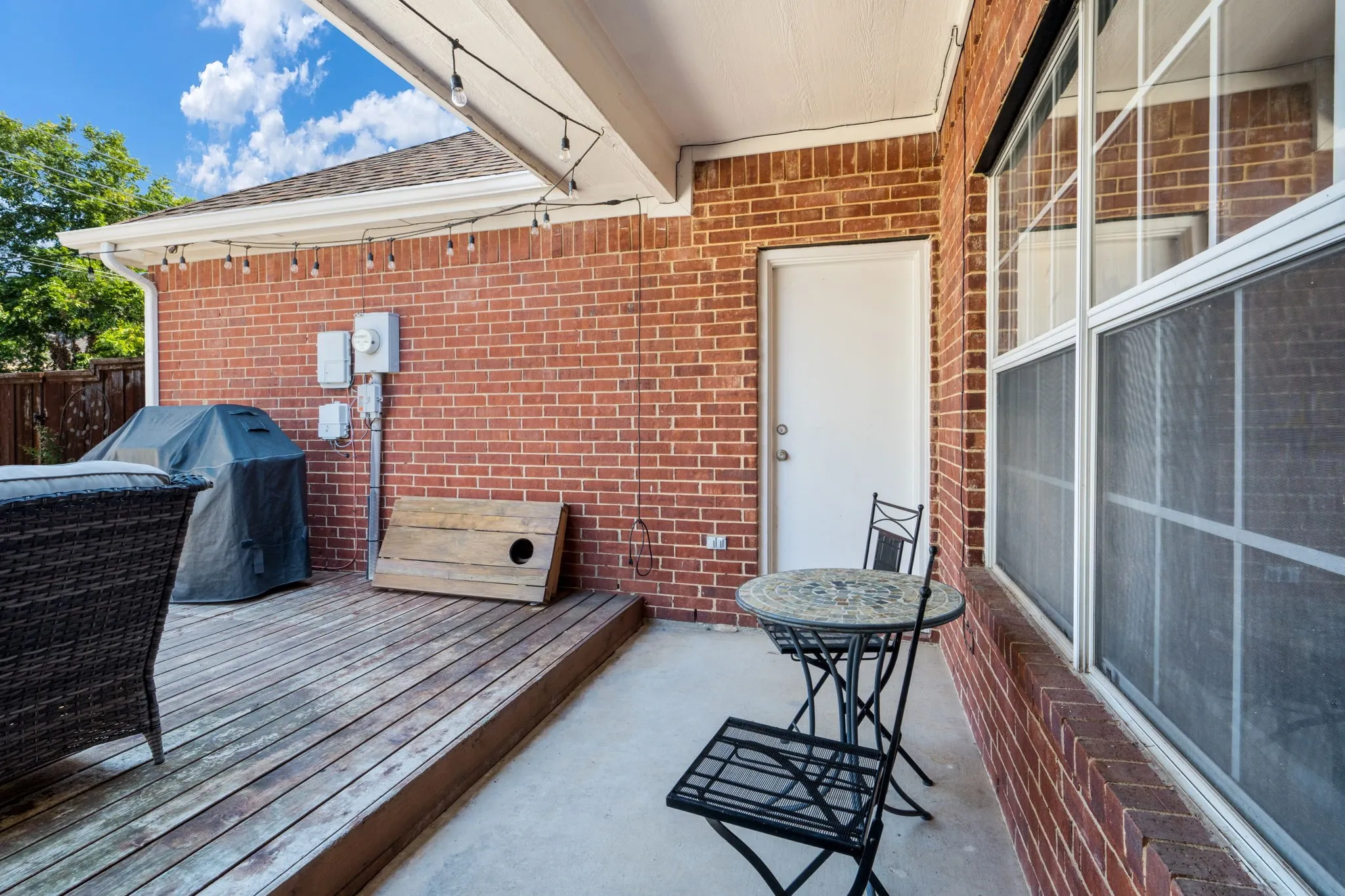Covered outdoor patio featuring brick exterior, wood-finish decking, and string lighting