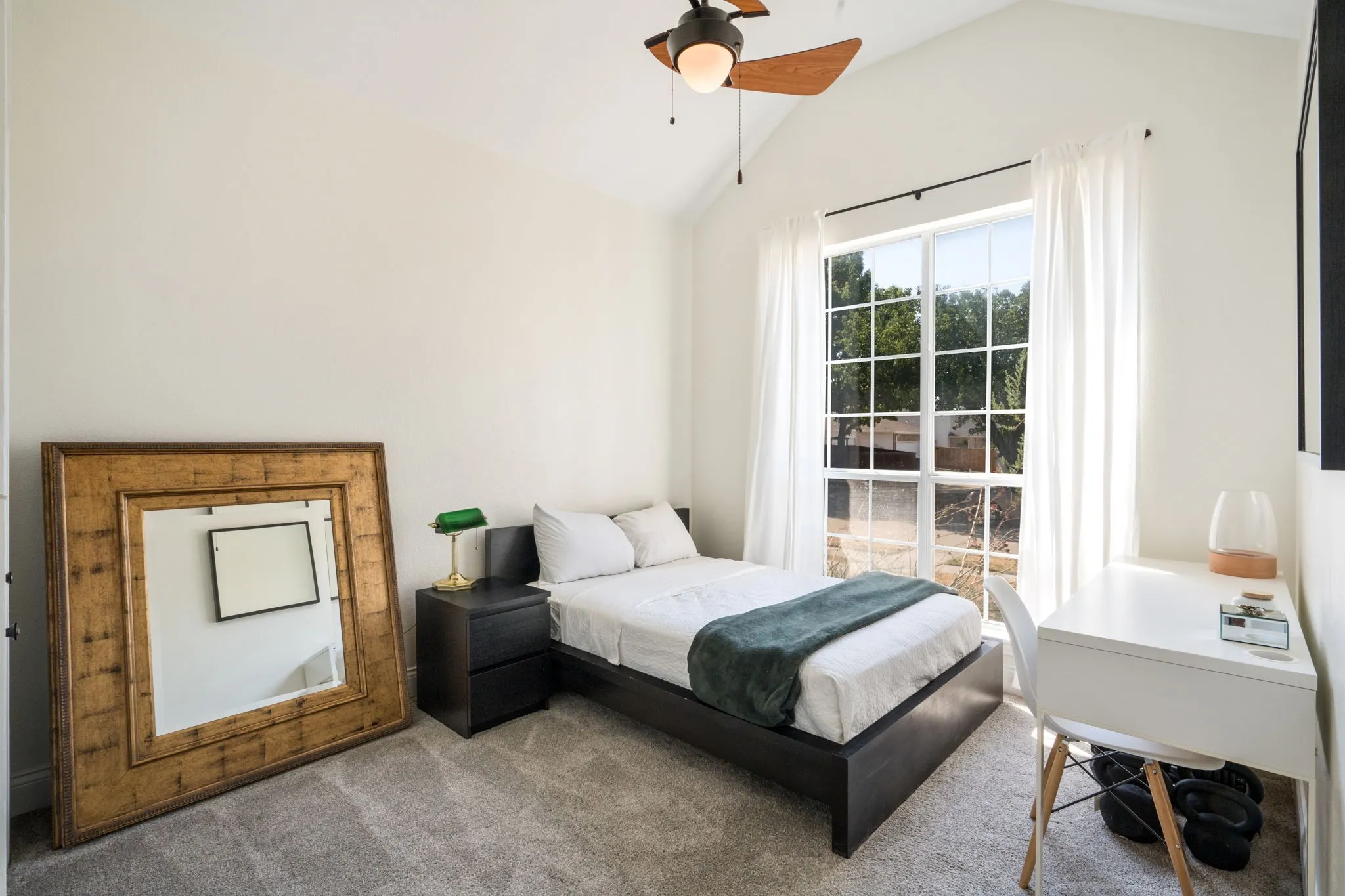 Vaulted ceiling with an attached ceiling fan, large multi-pane window with white curtains, and neutral wall paint