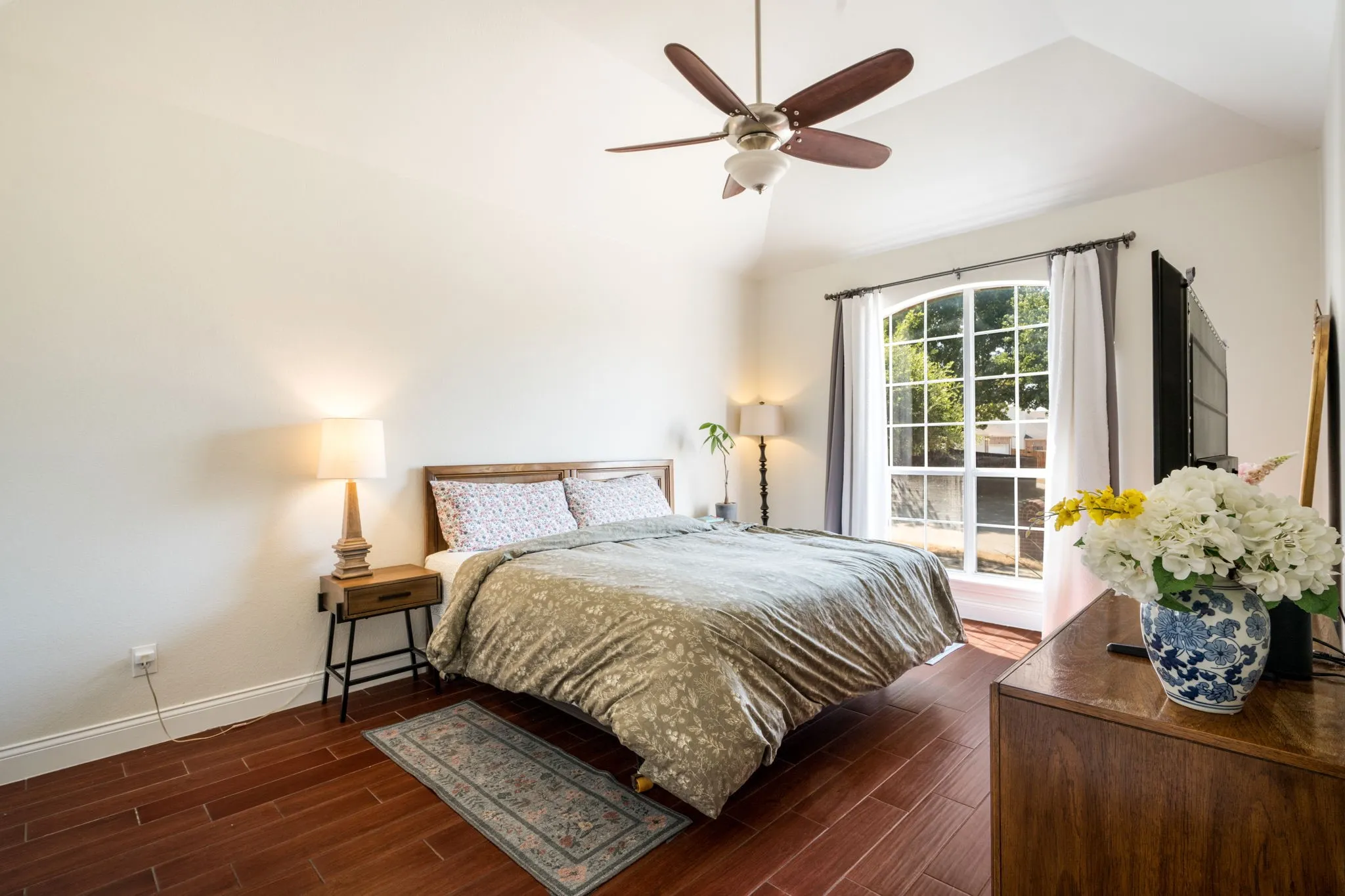 Vaulted ceiling with a ceiling fan, arched window, wood-finish flooring, and light-toned walls