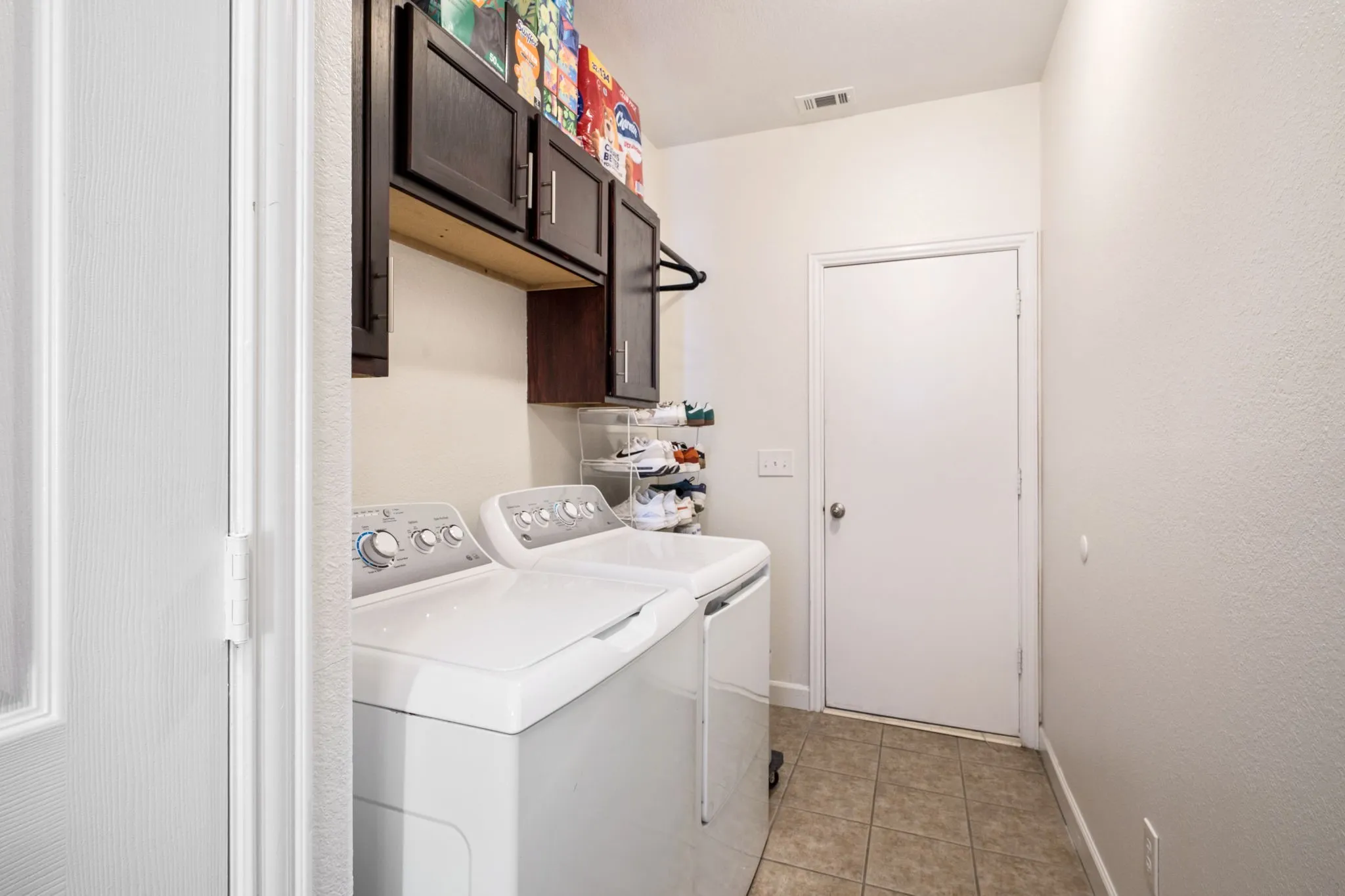 Laundry area featuring tile flooring, dark wood-finish cabinetry, and a built-in hanging rod