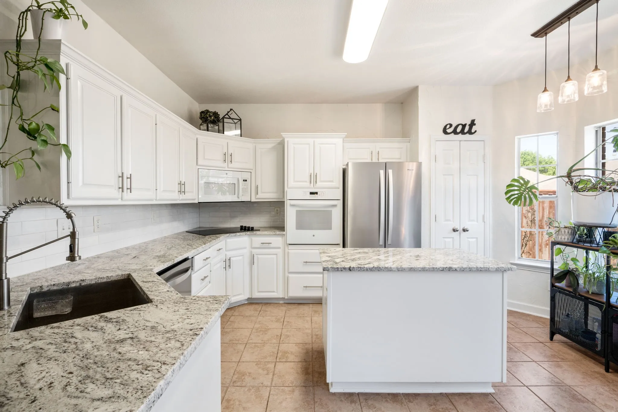 White cabinetry with brushed nickel hardware, light-toned granite countertops, a central island, stainless steel appliances, and tile flooring