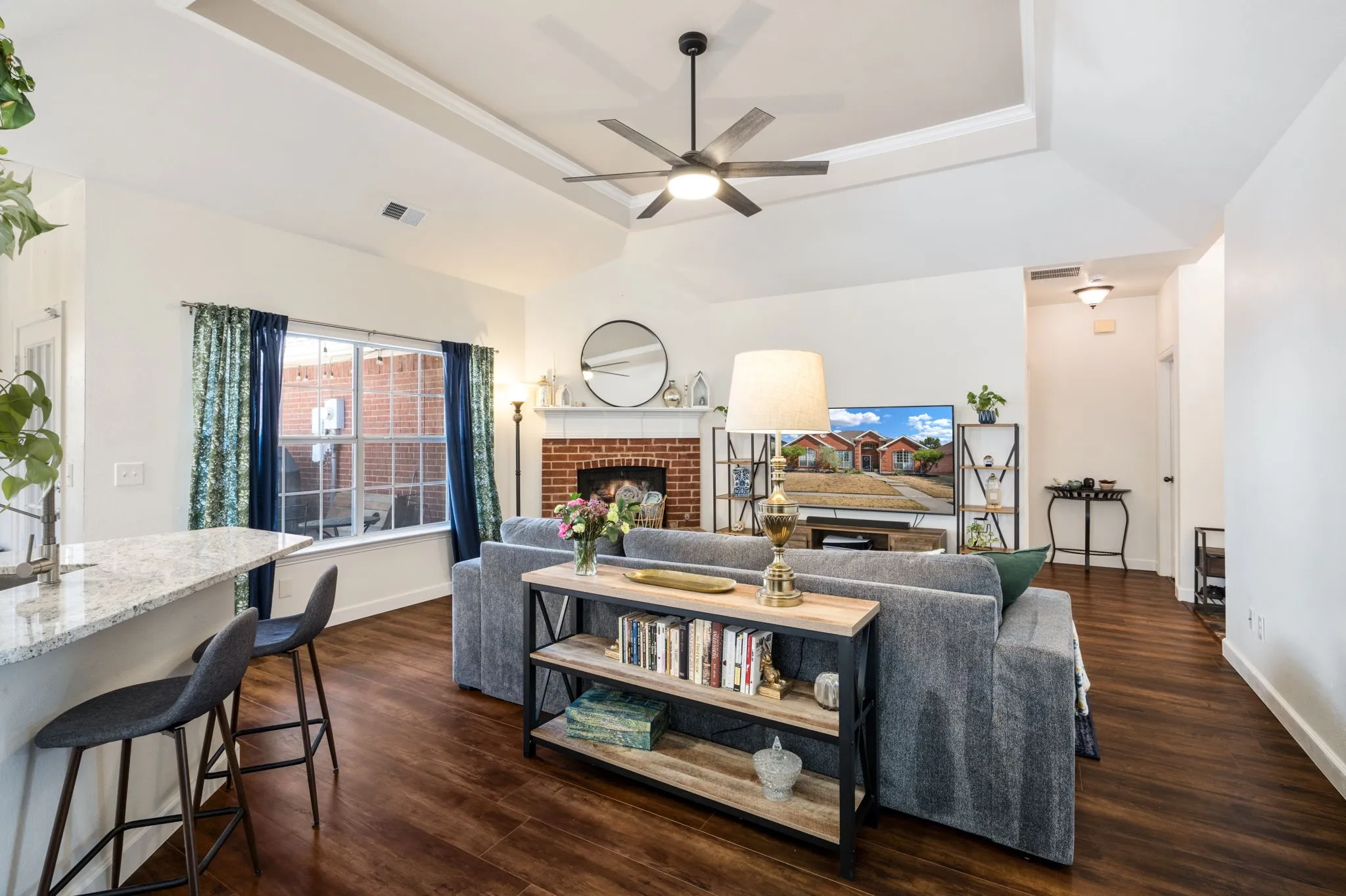 Open-concept living area with wood-finish flooring, a tray ceiling, and a ceiling fan