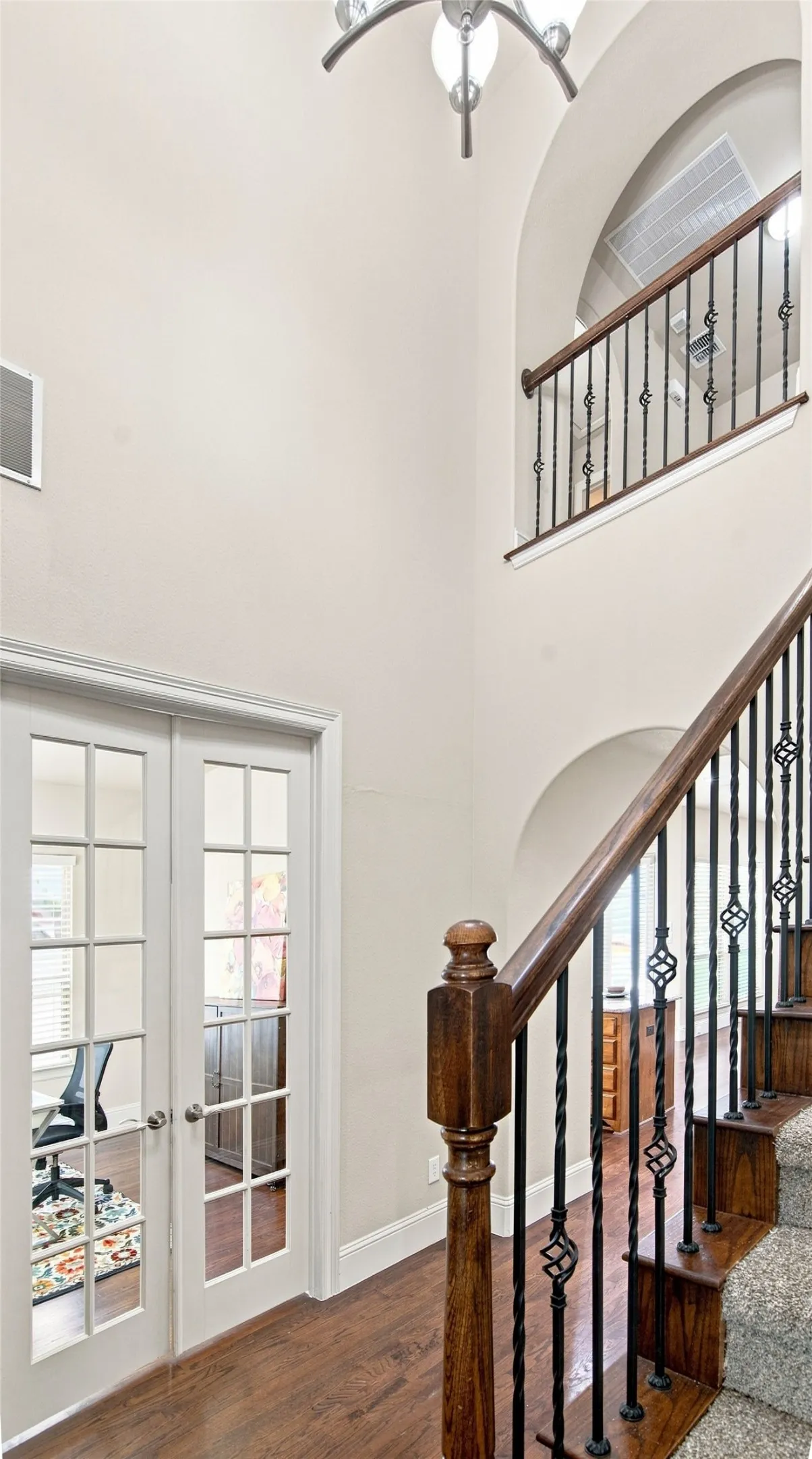 Two-story foyer with wood-finish flooring, wrought iron balusters, and a decorative chandelier