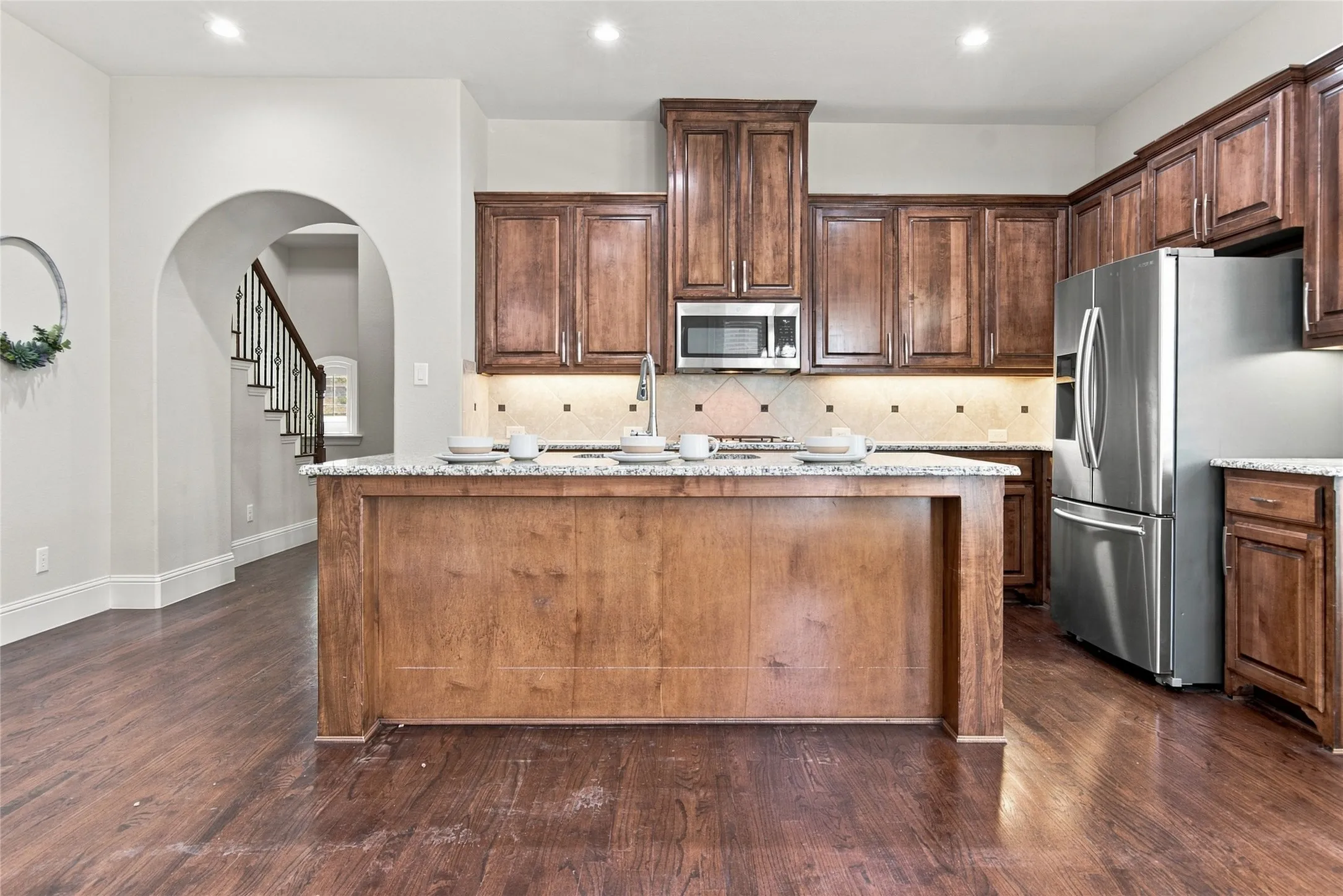 Kitchen featuring wood-finish flooring, recessed lighting, wood cabinetry, stainless steel appliances, and a central island with a stone countertop