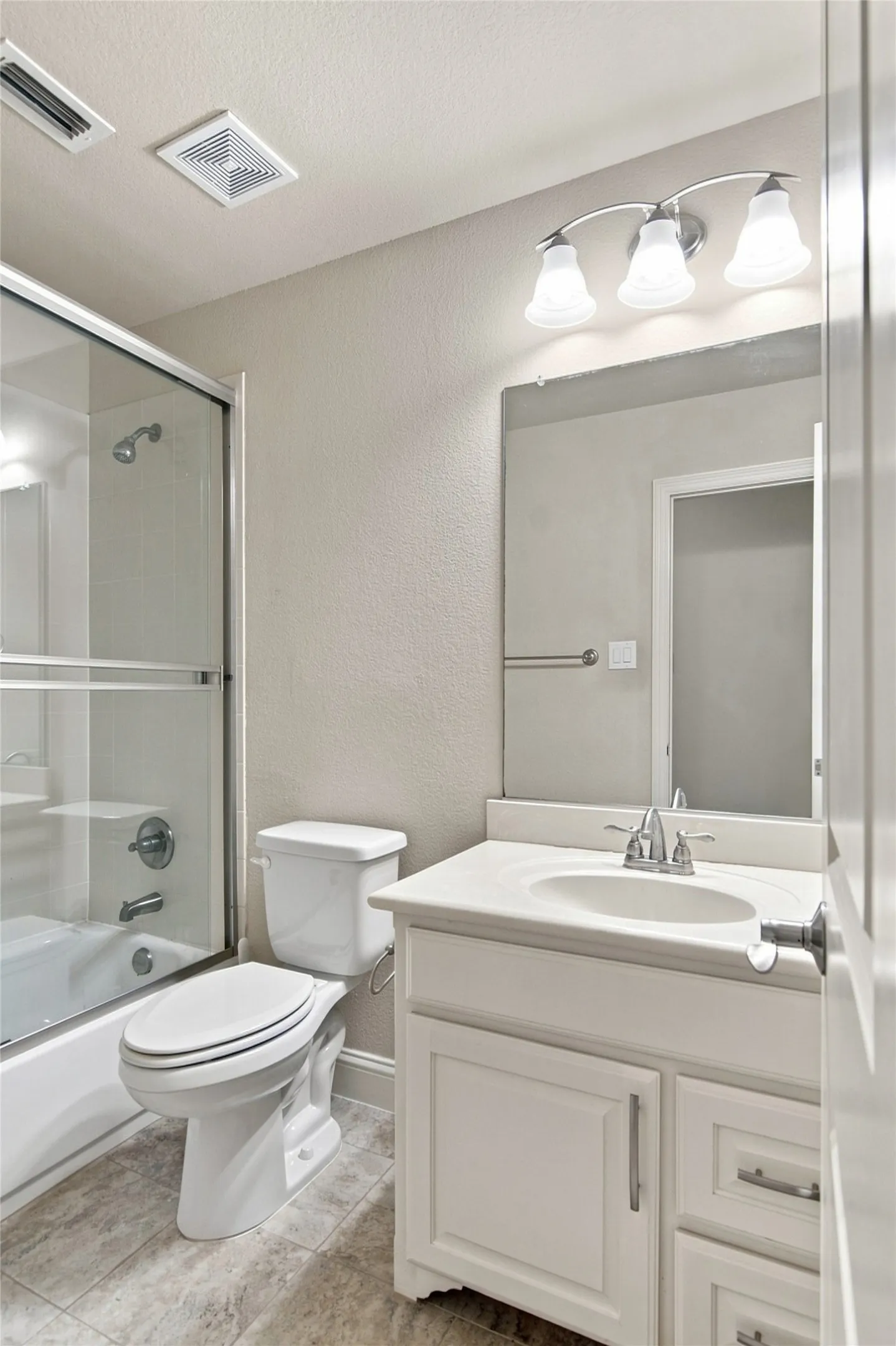 Shower-tub combination with glass enclosure, white vanity with integrated sink, chrome faucet, and vanity lighting