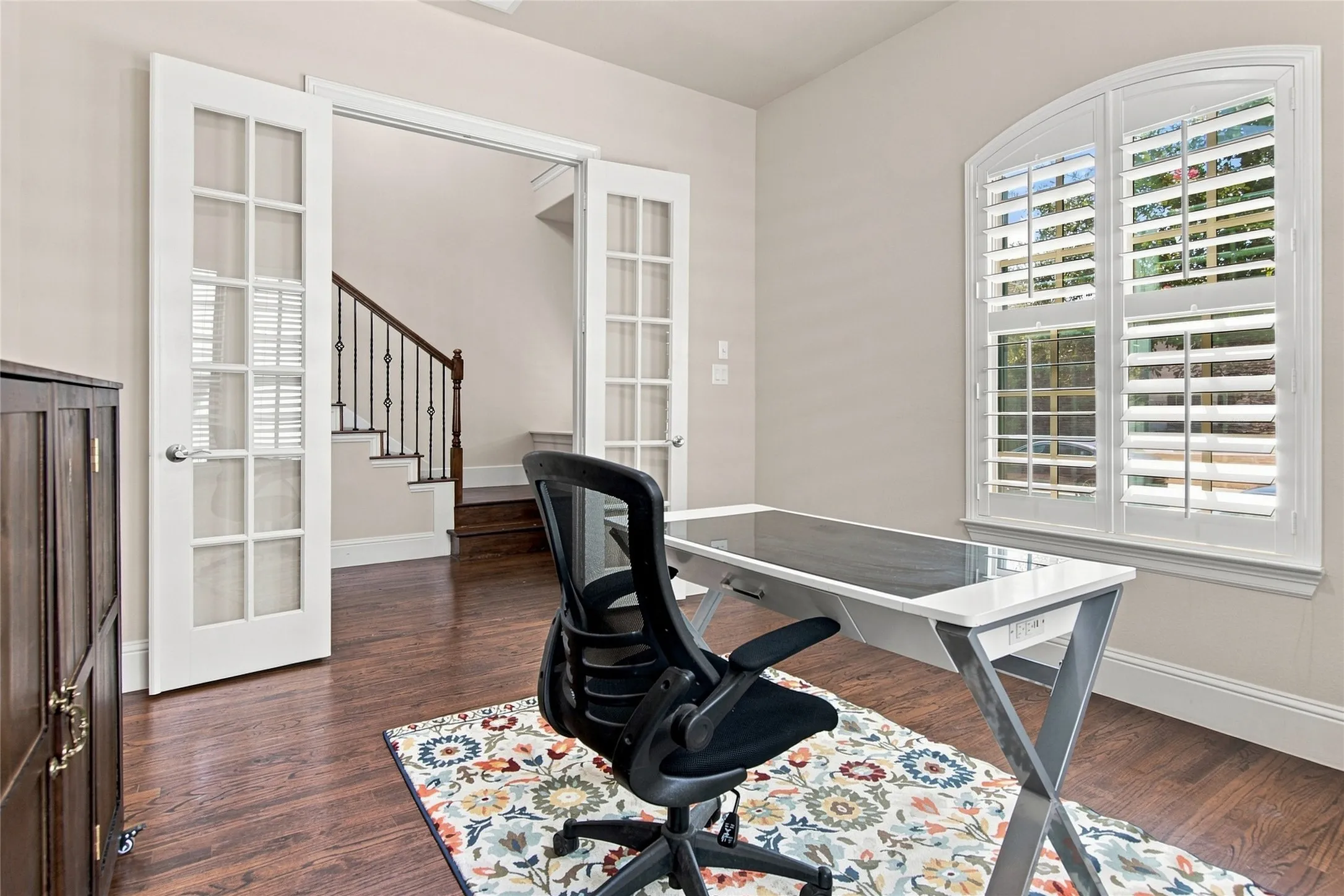 Hardwood-finish flooring, white plantation shutters, arched window, and double French doors