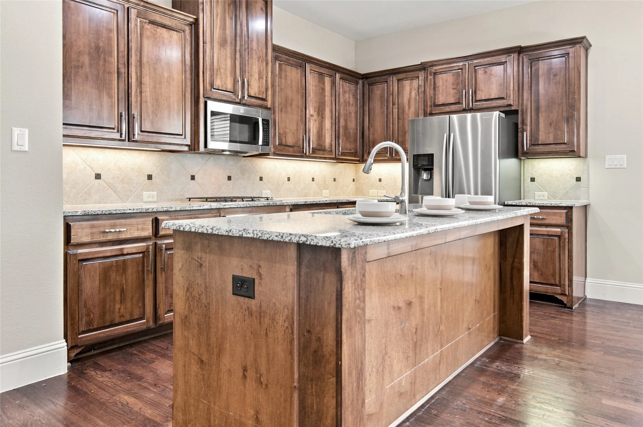 Kitchen featuring wood cabinetry, granite countertops, stainless steel appliances, a tile backsplash, and a central island with a sink
