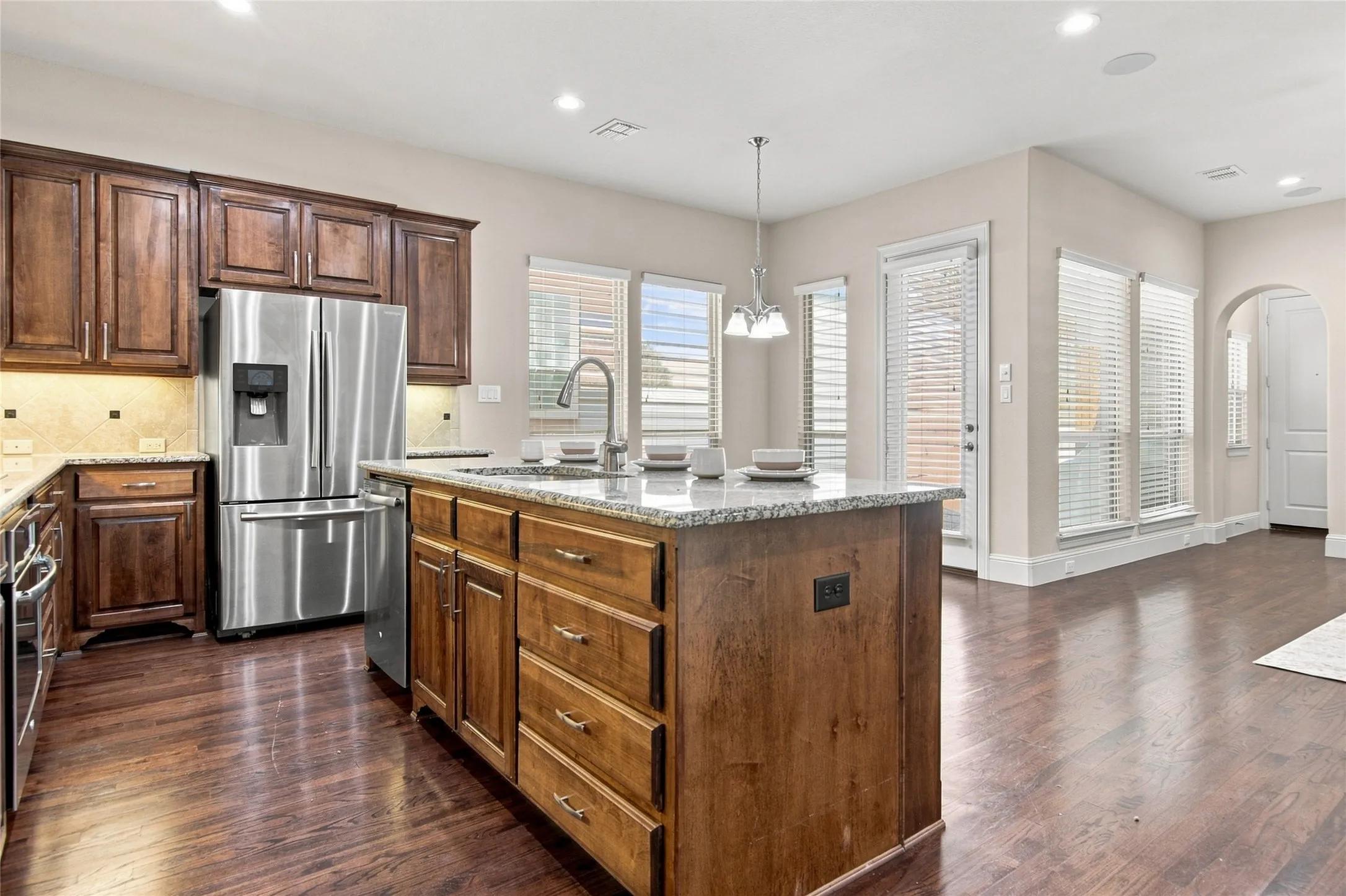 Kitchen featuring wood cabinetry, stainless steel appliances, a center island with a sink, and wood-finish flooring