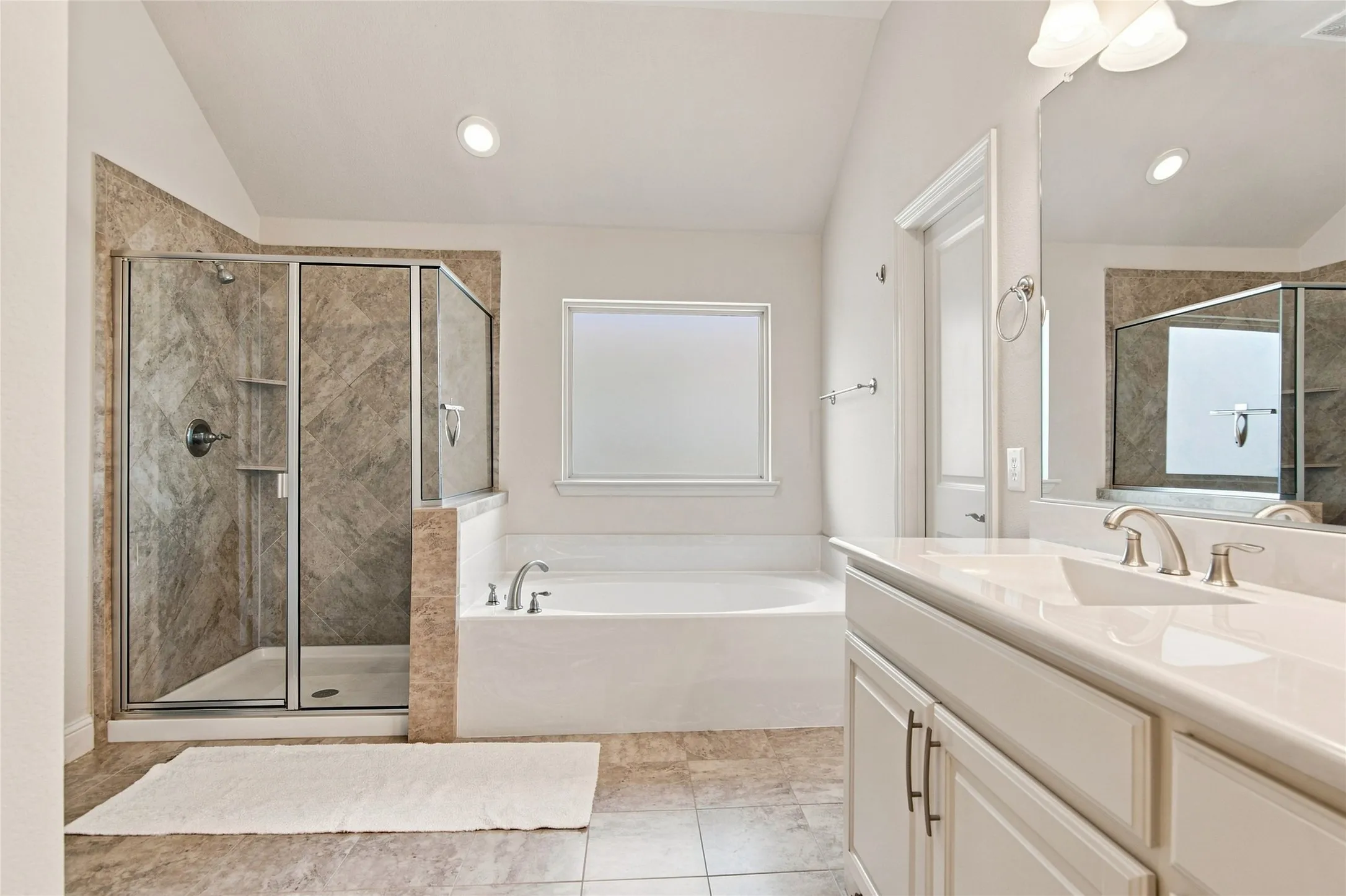 Walk-in shower with glass enclosure, separate soaking tub, dual vanity with undermount sinks, and stone-look tile flooring