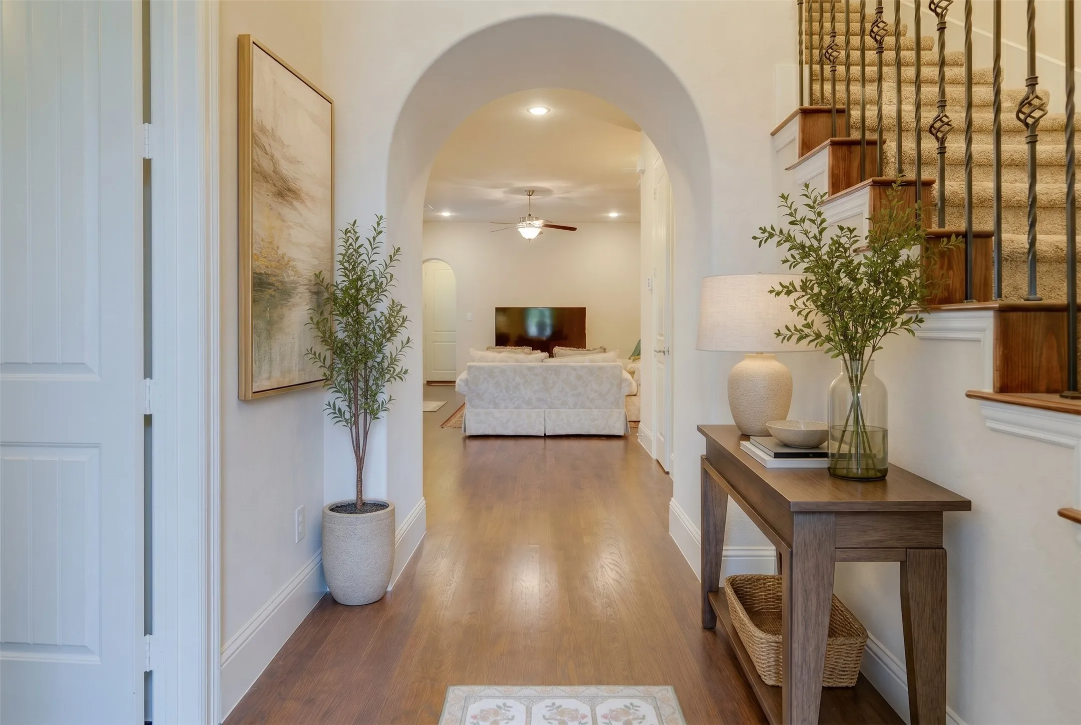 Hardwood-finish flooring, arched entryway, staircase with wrought iron balusters, recessed lighting, and crown molding