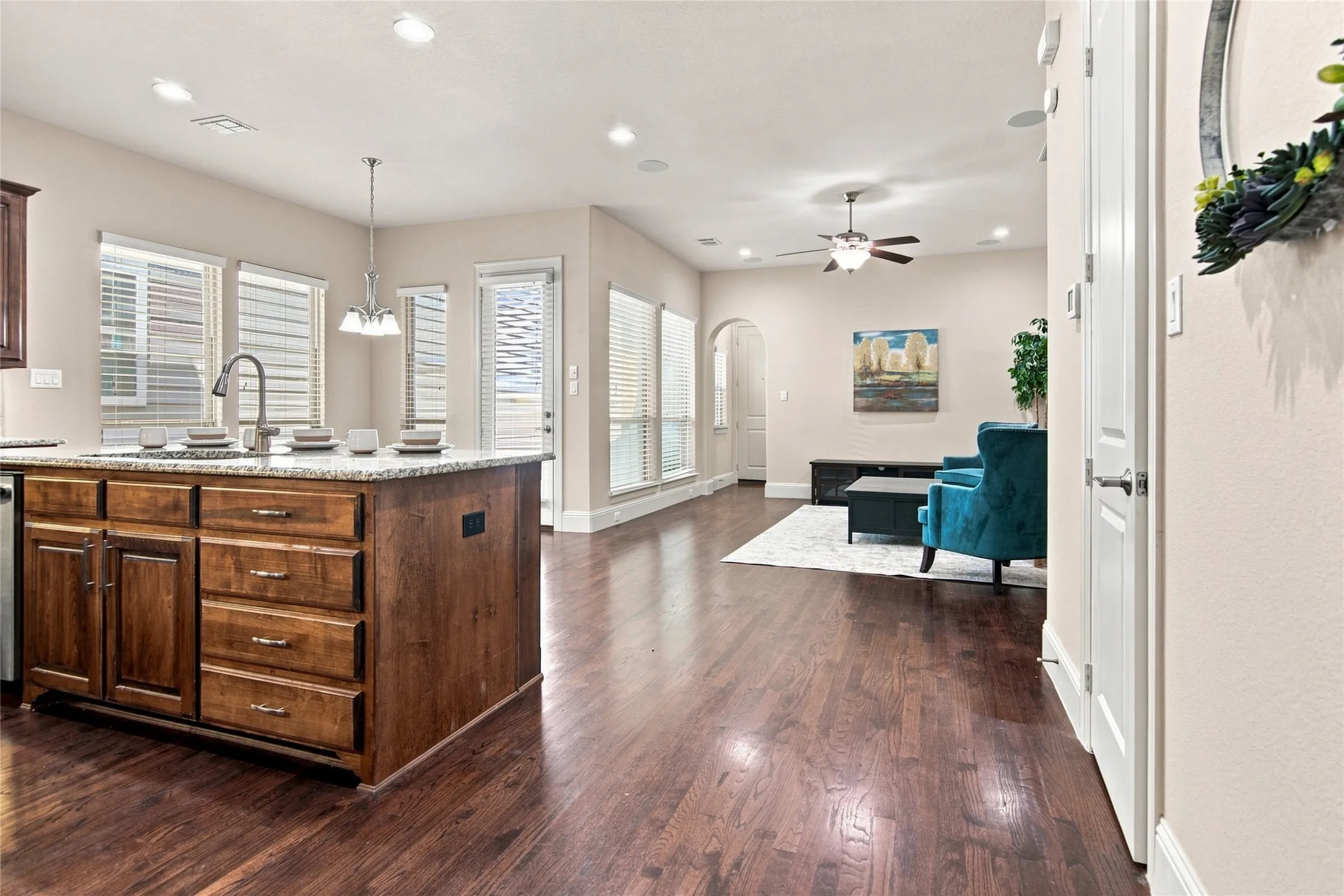 Open-concept living space featuring wood-finish flooring, a kitchen island with stone countertops, recessed lighting, and a ceiling fan
