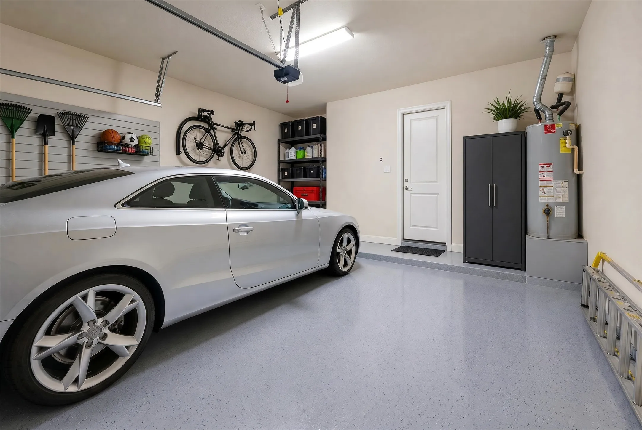 Garage featuring epoxy flooring, wall-mounted storage system, overhead lighting, and built-in shelving