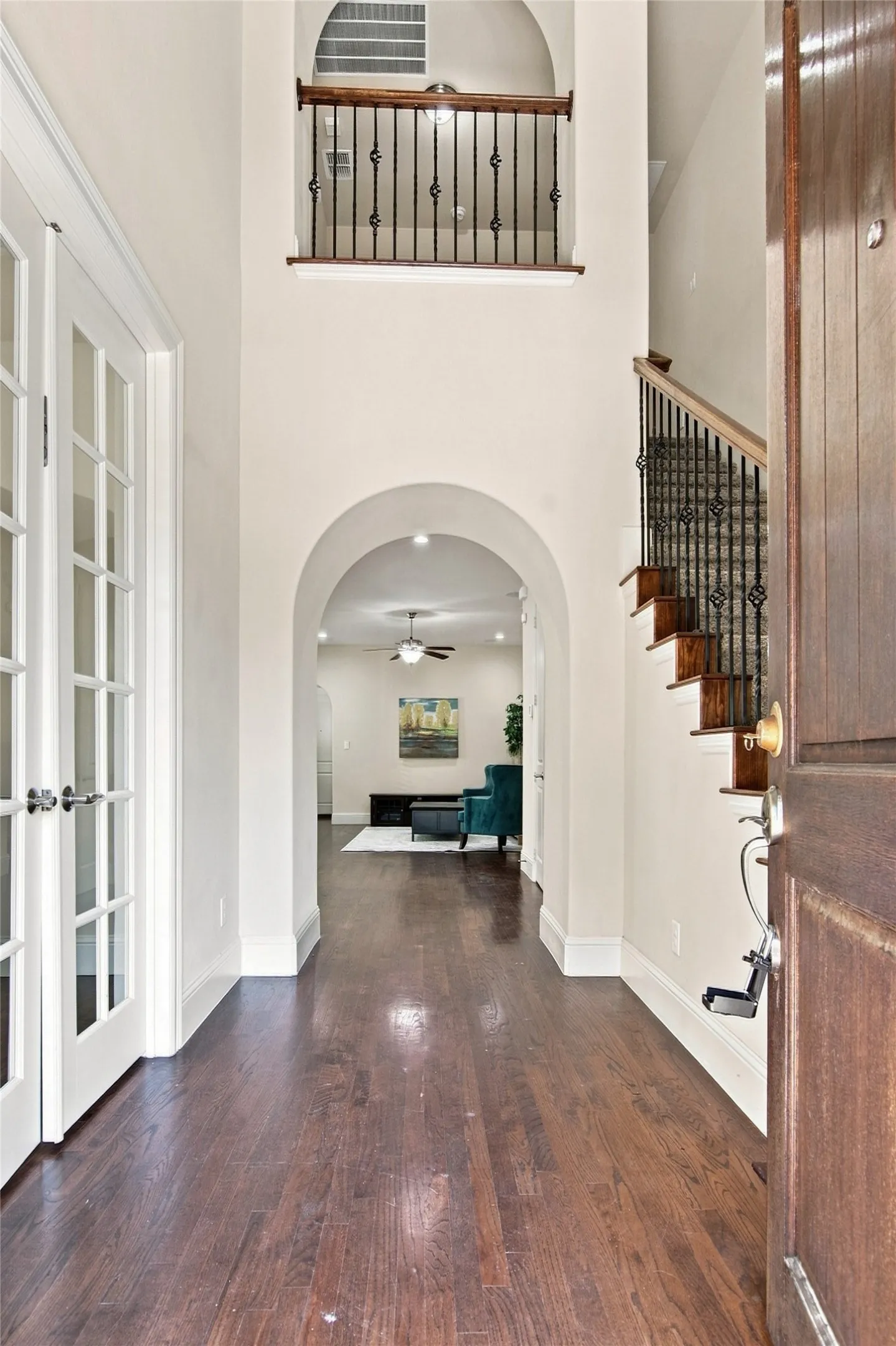 Two-story foyer featuring dark wood-finish flooring, an arched entryway, French doors, and an iron baluster staircase