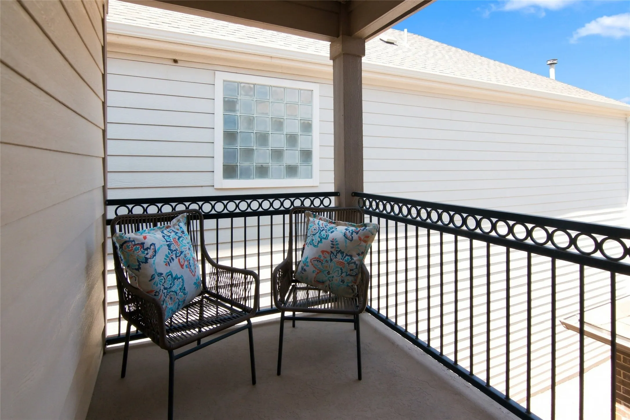 Private balcony featuring a decorative wrought iron railing, concrete flooring, and a glass block window