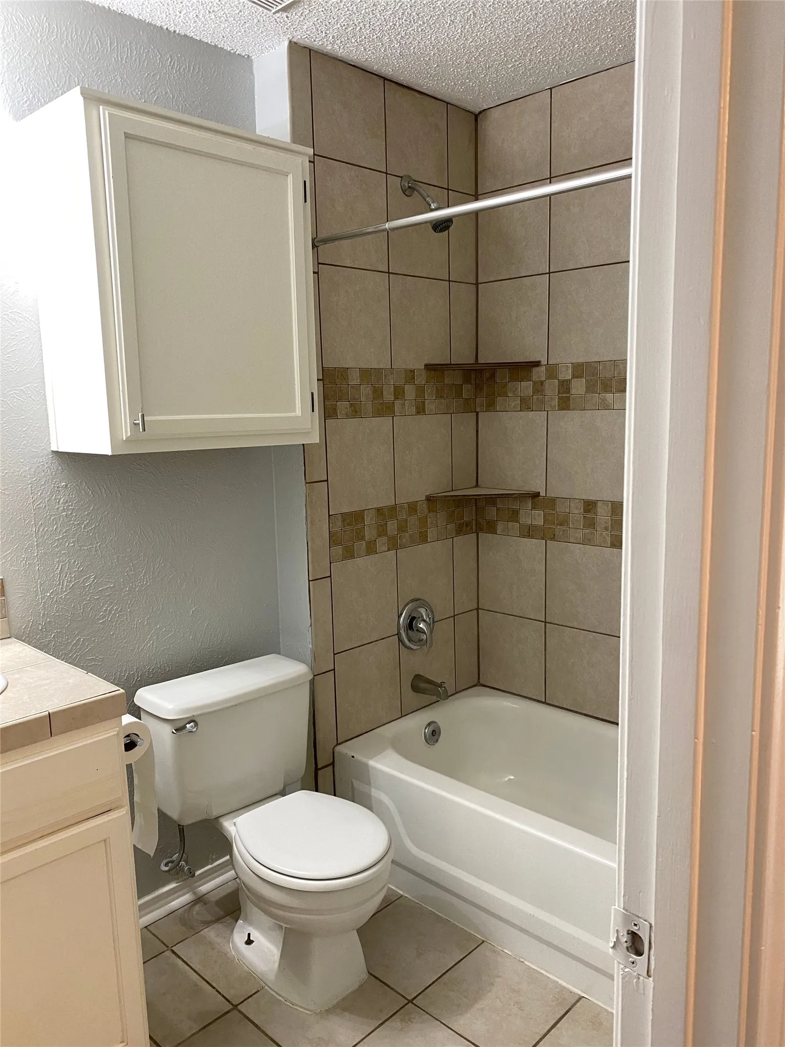 Bathtub with full tile surround, decorative tile band, and built-in corner shelving