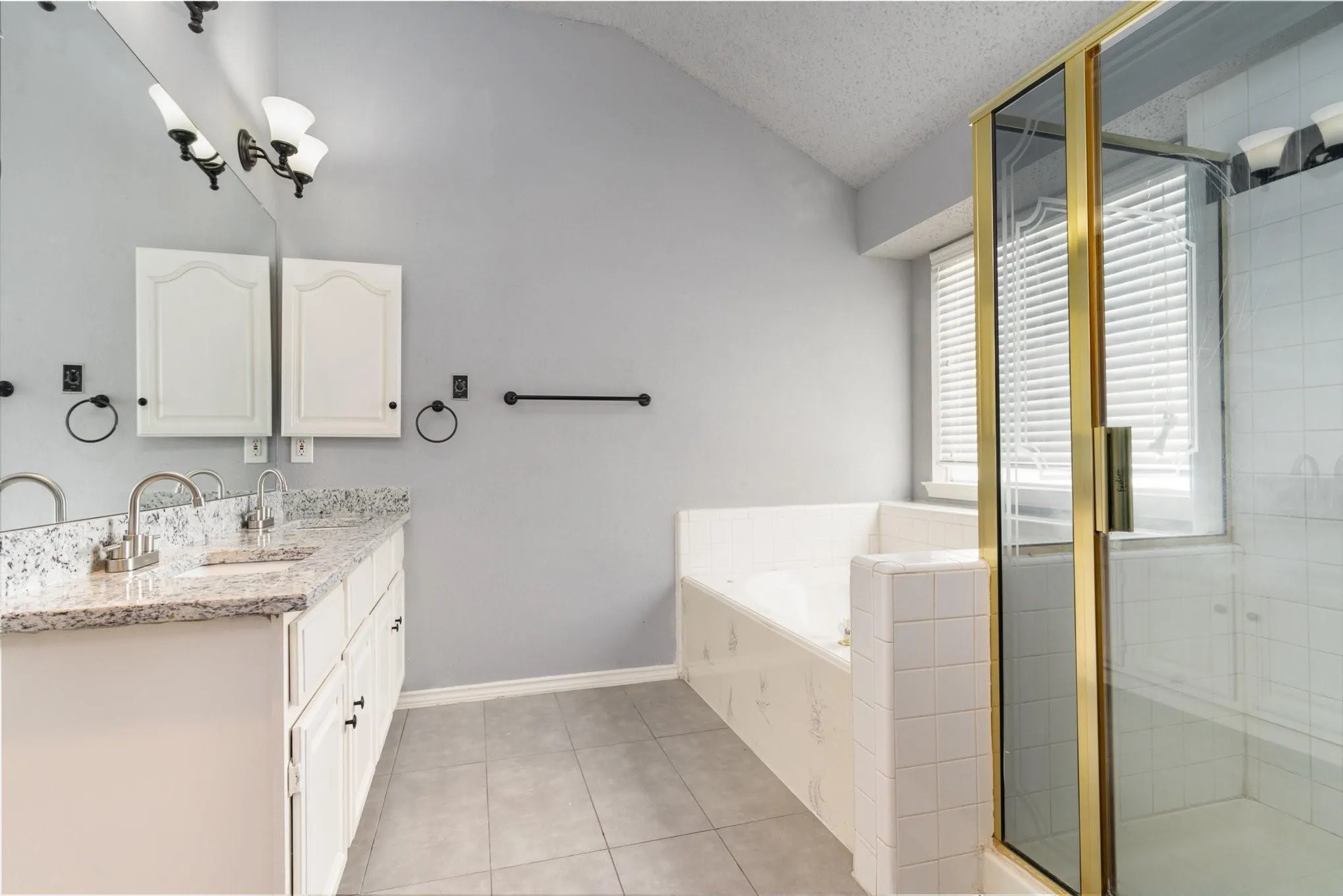 Dual vanity with granite-style countertop, white cabinetry, integrated soaking tub, and a glass-enclosed shower