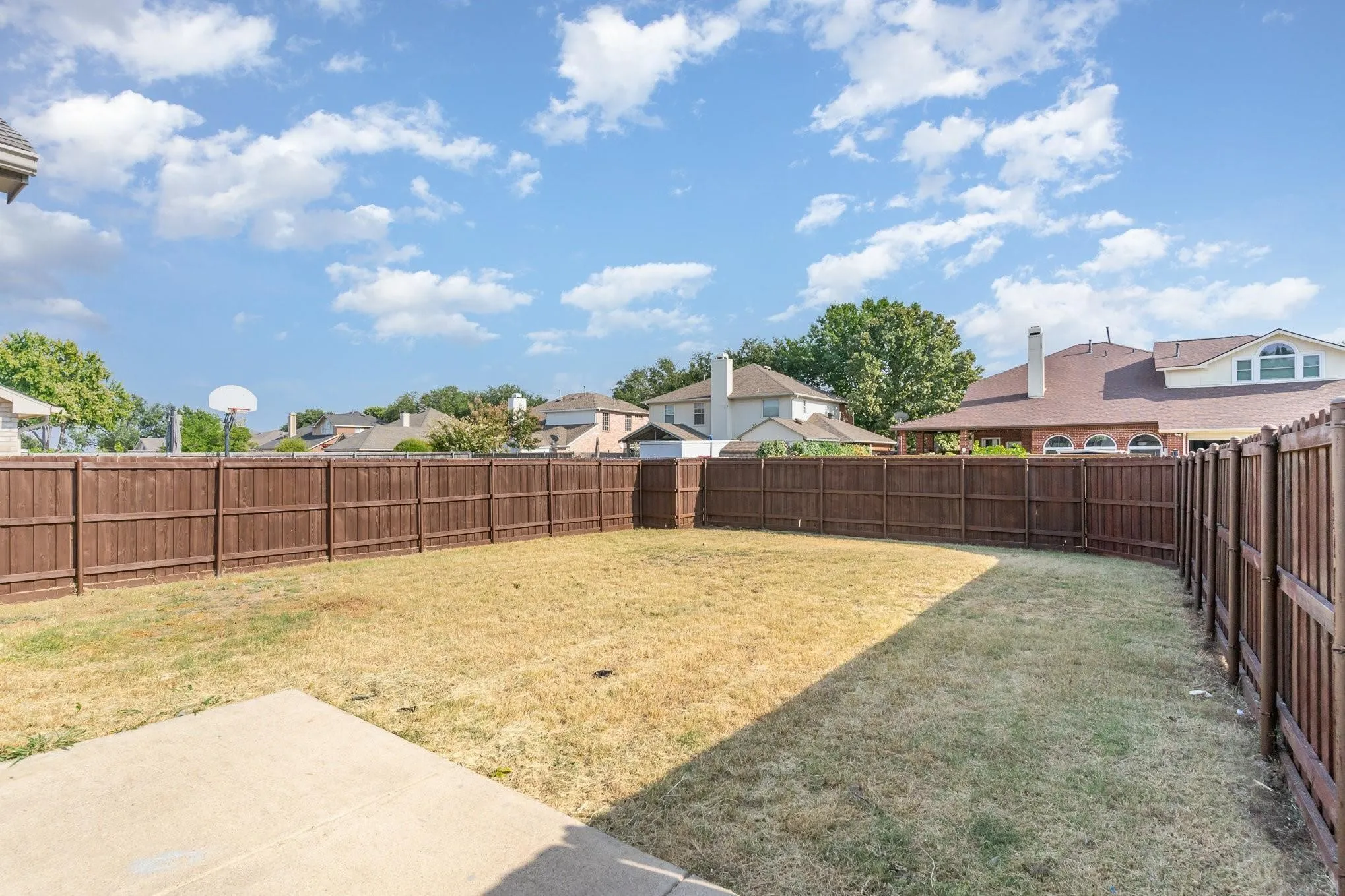 Expansive outdoor area featuring a wood fence, concrete patio, and mature trees