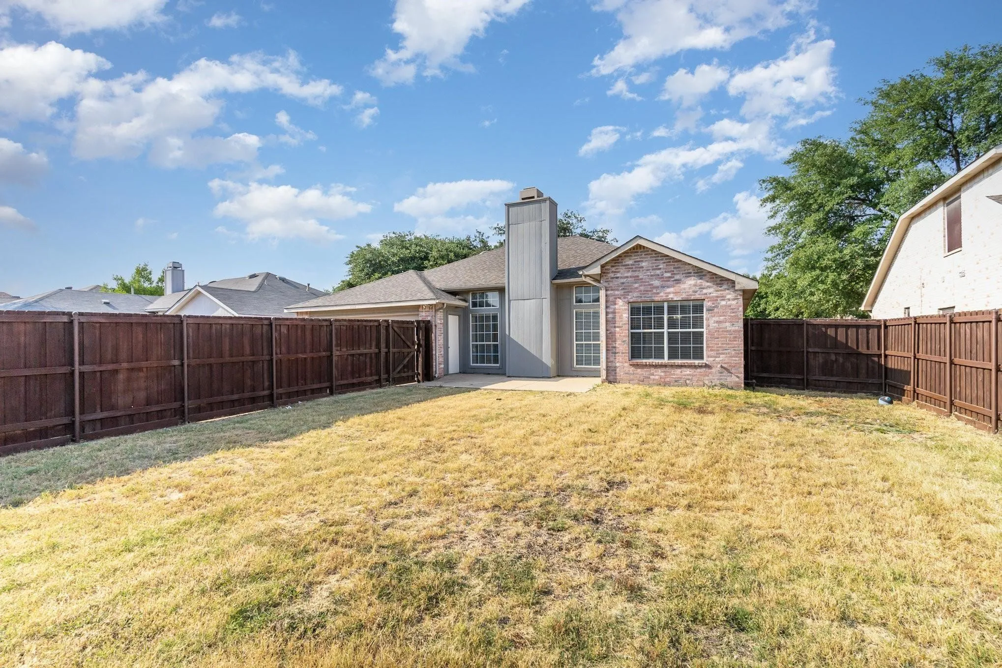 Expansive backyard featuring a privacy fence, concrete patio, and brick exterior