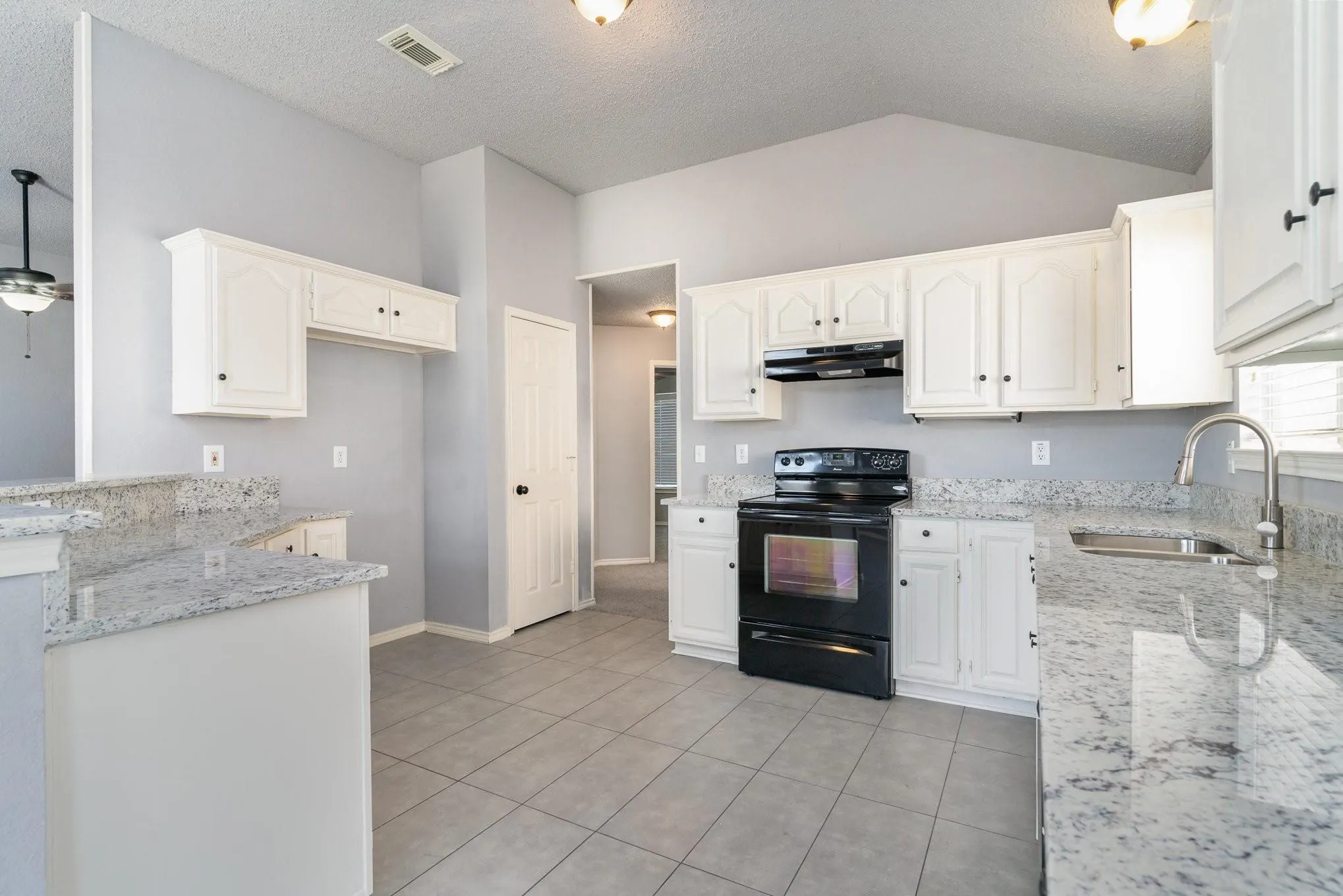 Kitchen with vaulted ceilings, white cabinetry, a built-in electric range, granite countertops, and tile flooring