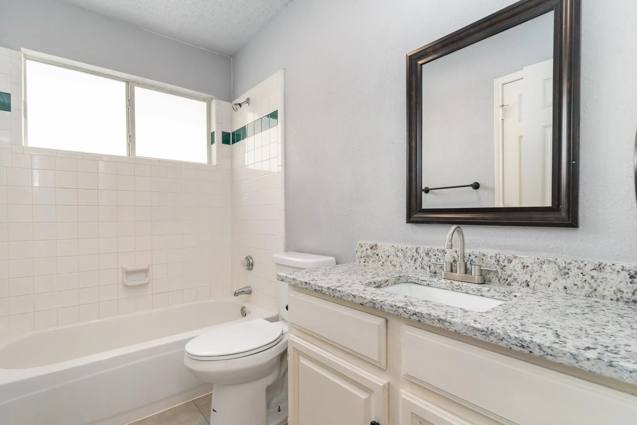 White vanity with a speckled countertop, framed mirror, and a built-in bathtub with tiled surround