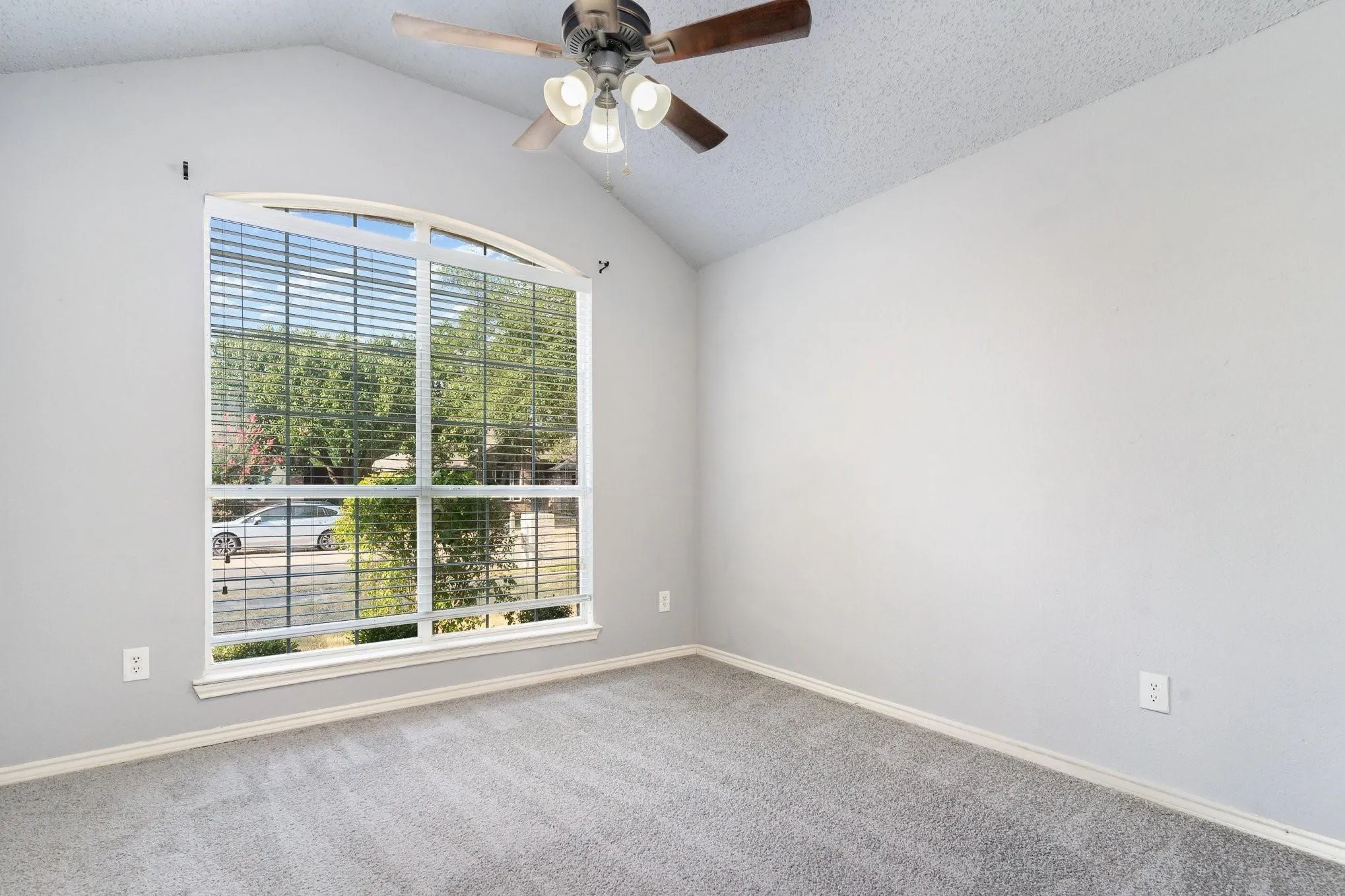 Vaulted ceiling with an attached ceiling fan, arched window, and gray carpeting
