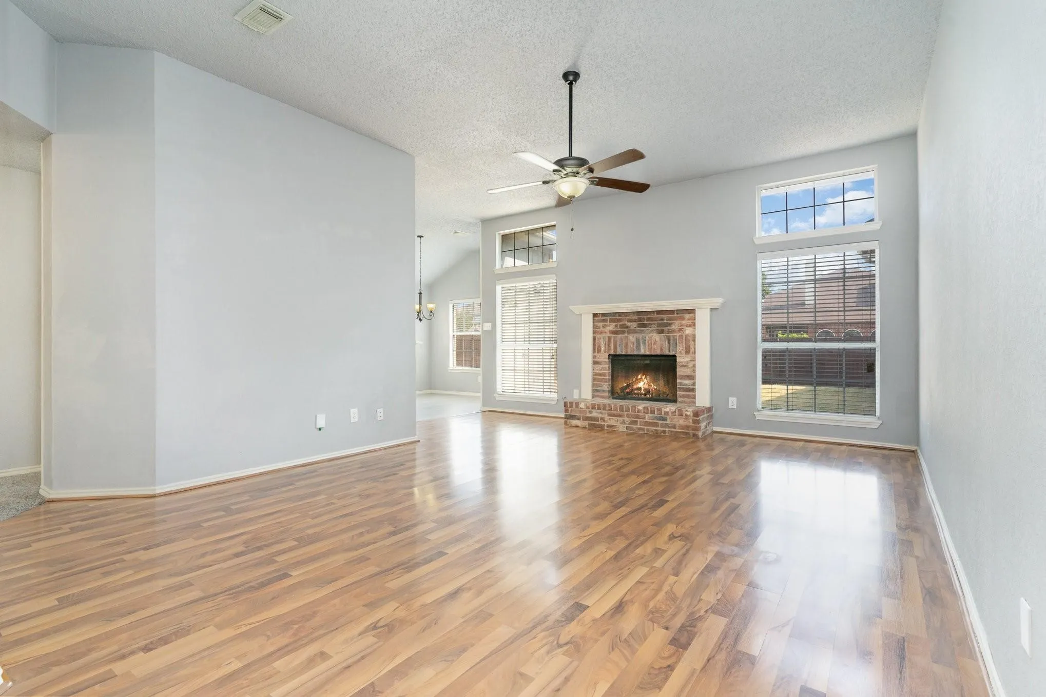 Wood-finish flooring, brick fireplace with a mantel, vaulted ceiling, ceiling fan with light fixture, and transom windows