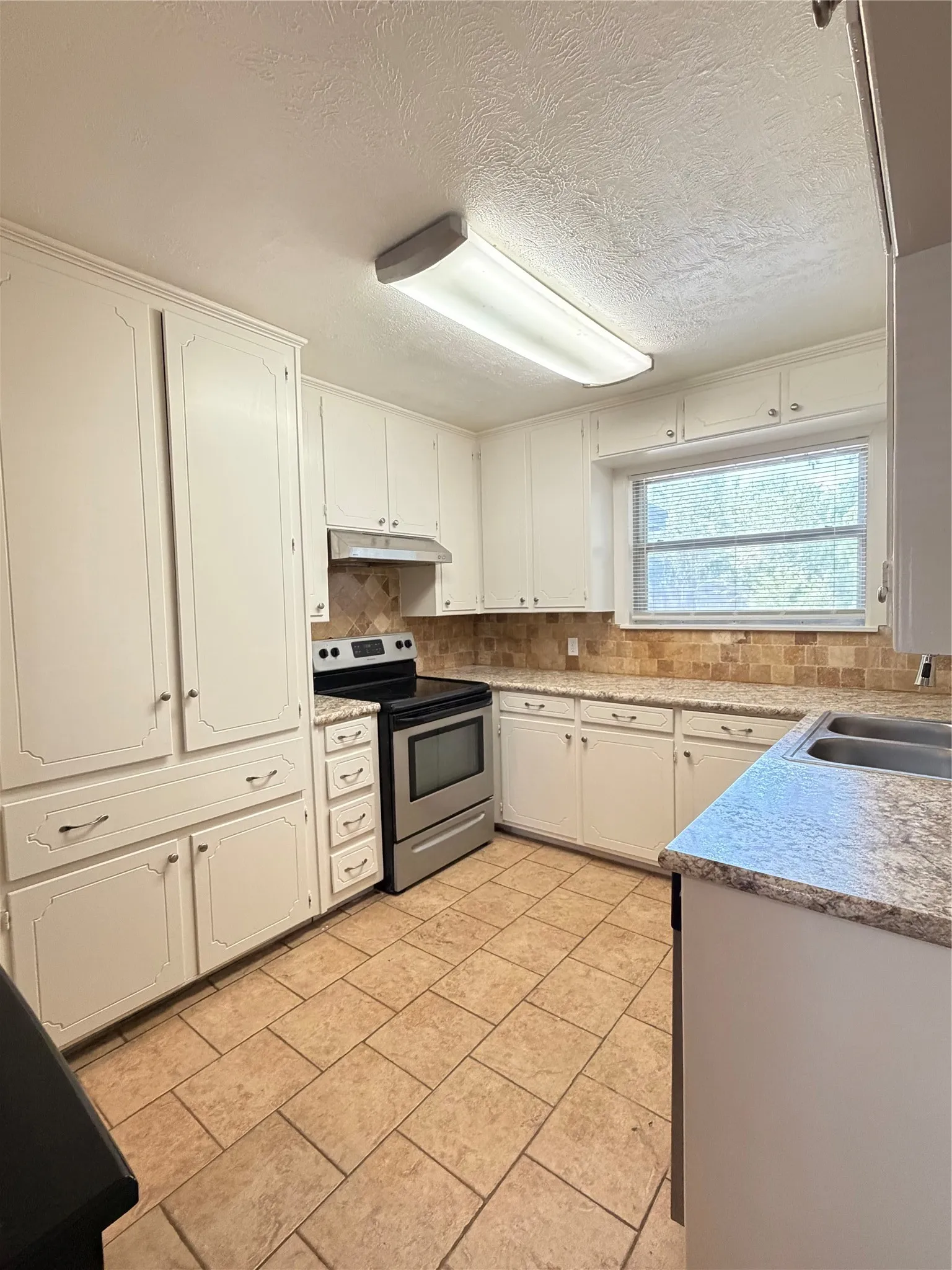 Recessed panel cabinetry, stainless steel range, tiled backsplash, dual basin sink, and tile flooring