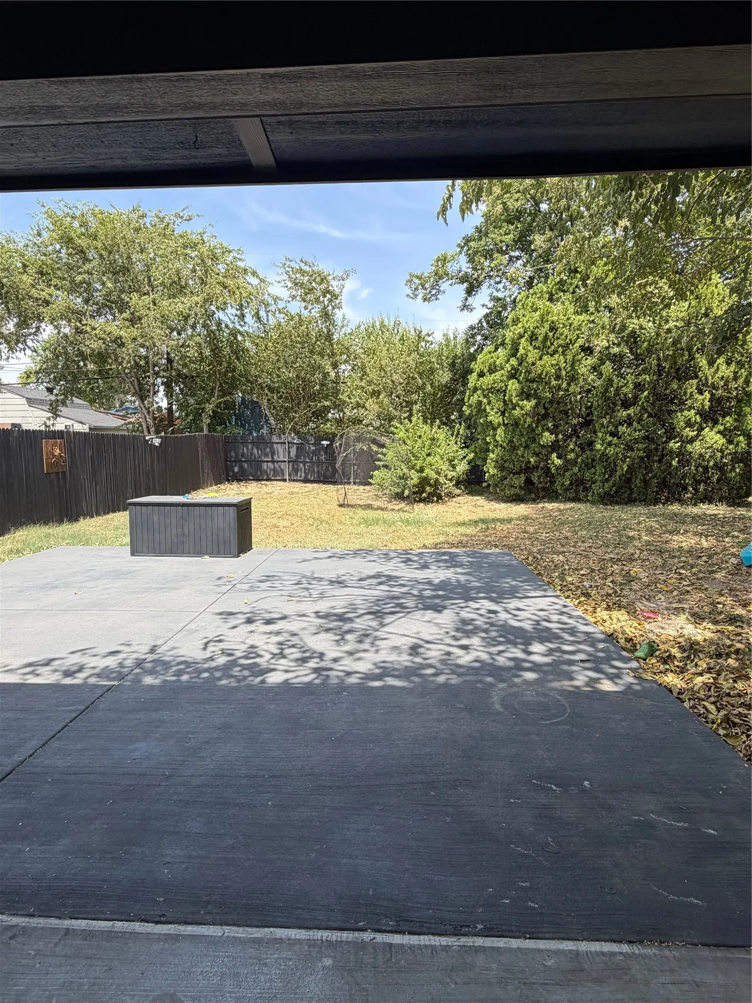 Expansive concrete patio with a privacy fence and mature trees