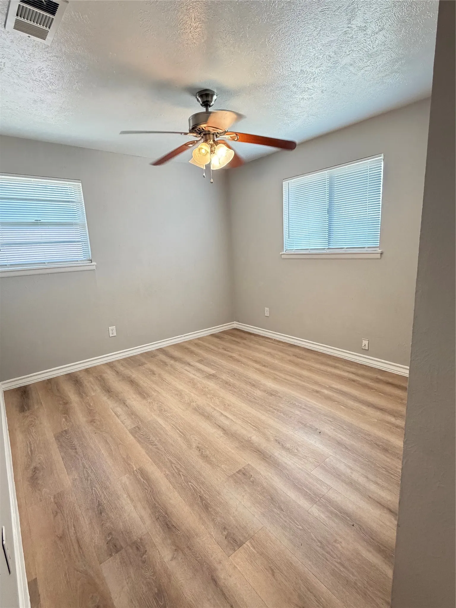 Wood-finish flooring, two windows with blinds, ceiling fan with light fixture, and neutral wall tones