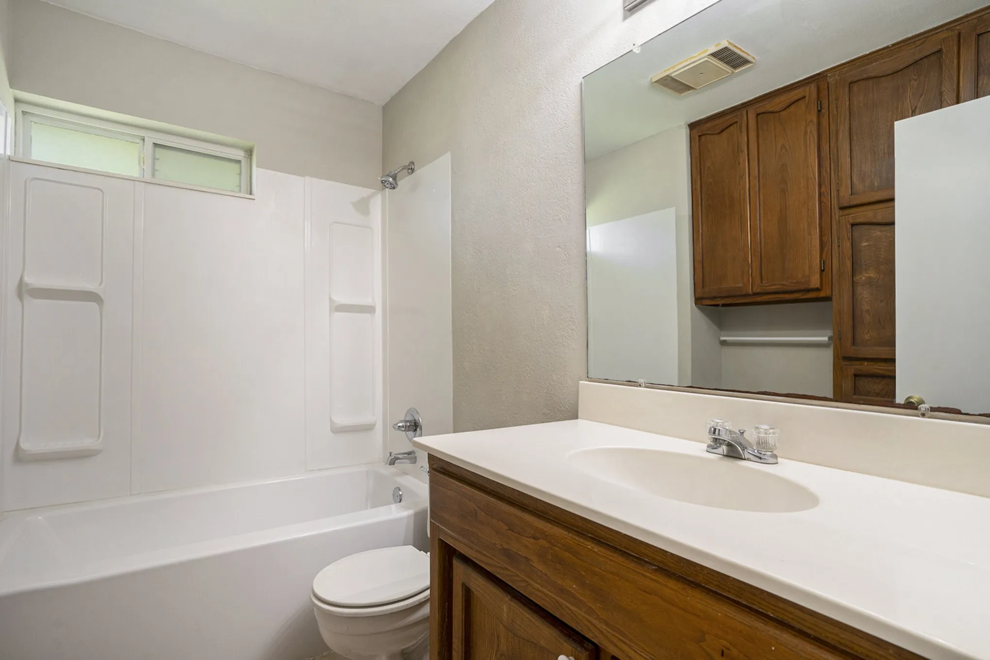 White bathtub with a shower, wood-finish vanity with an integrated sink, and an overhead mirror