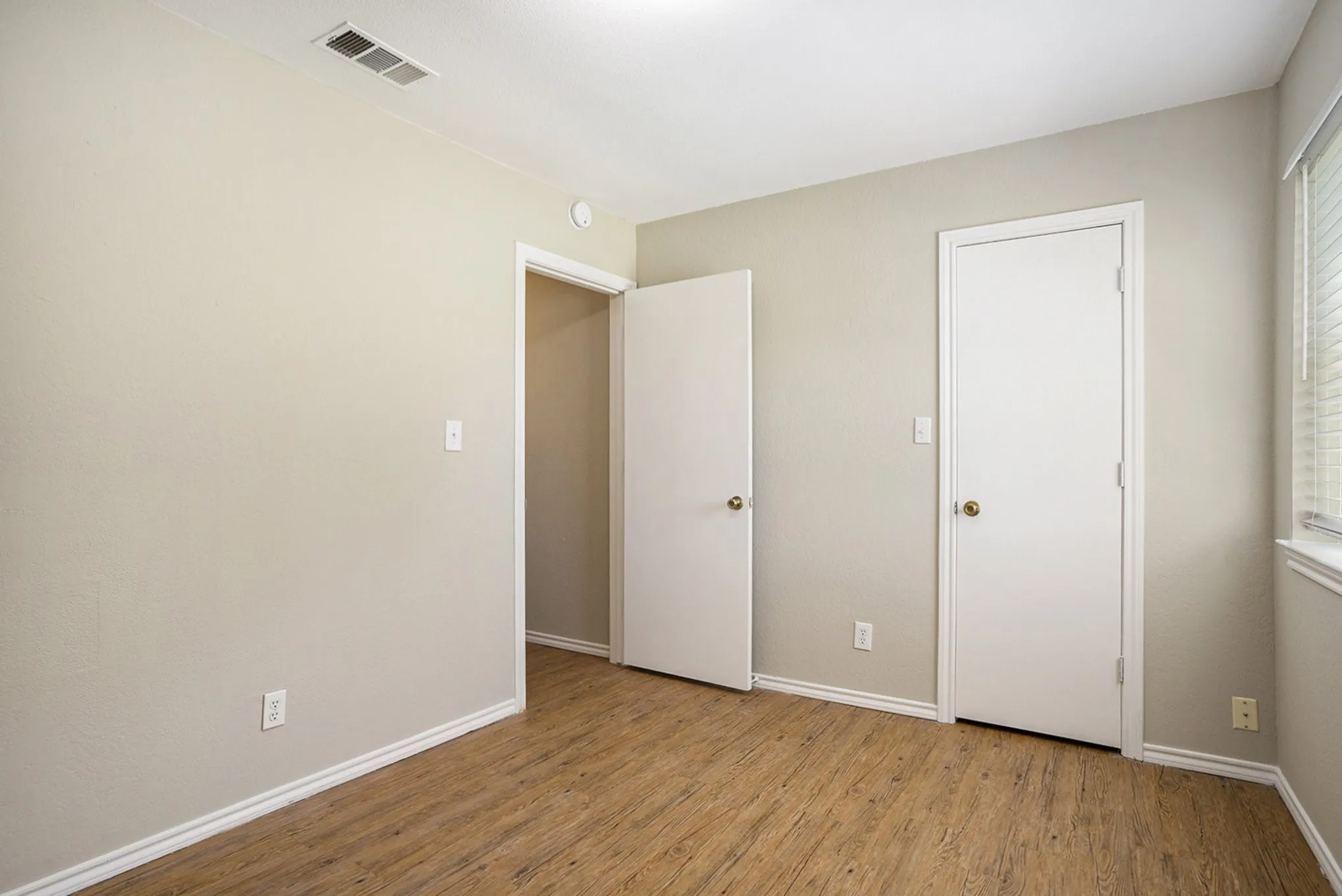 Wood-finish flooring, neutral wall paint, white trim, and window with blinds