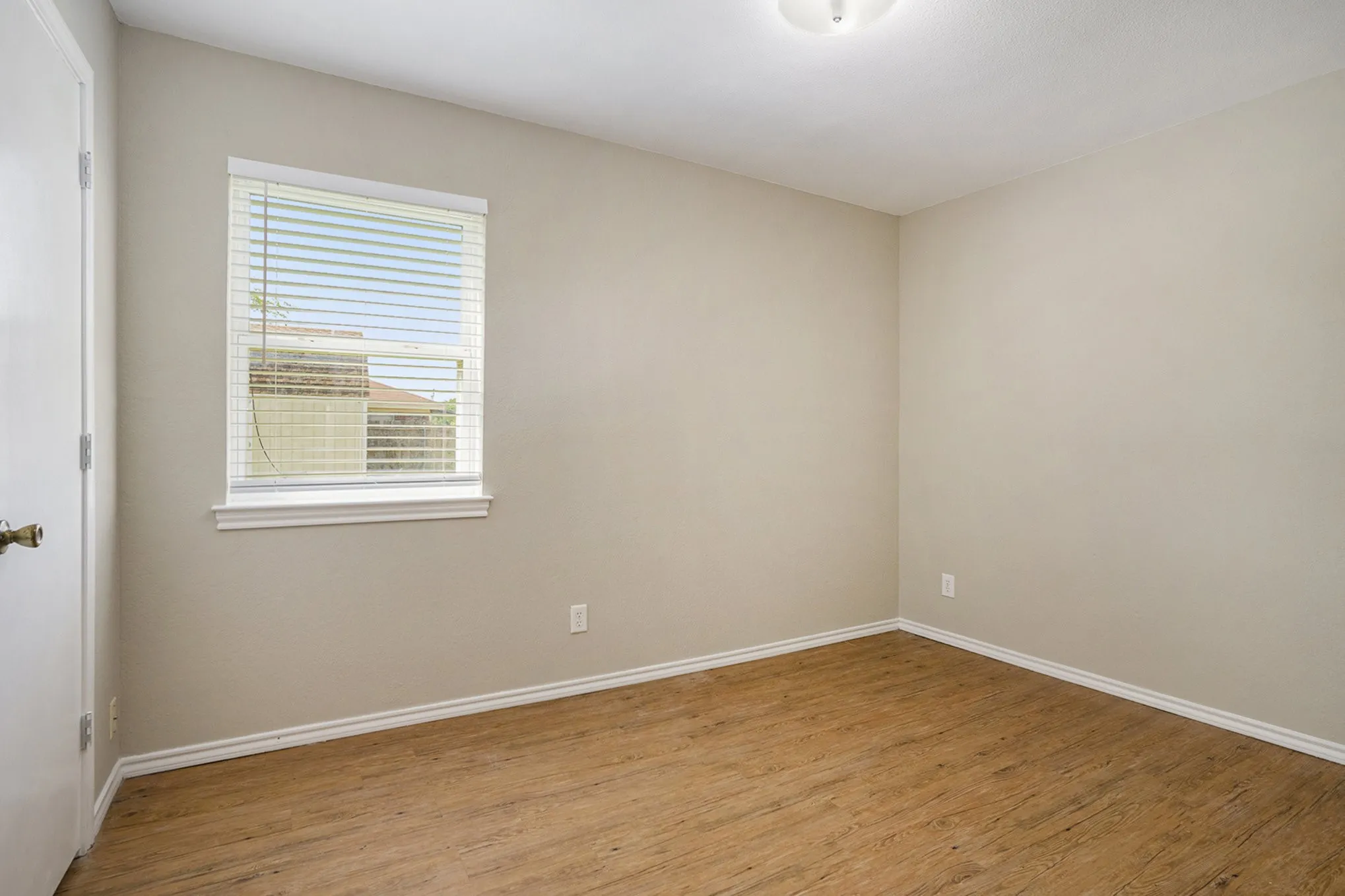 Wood-finish flooring, neutral wall tones, window with white blinds, white trim, and a flush mount ceiling light