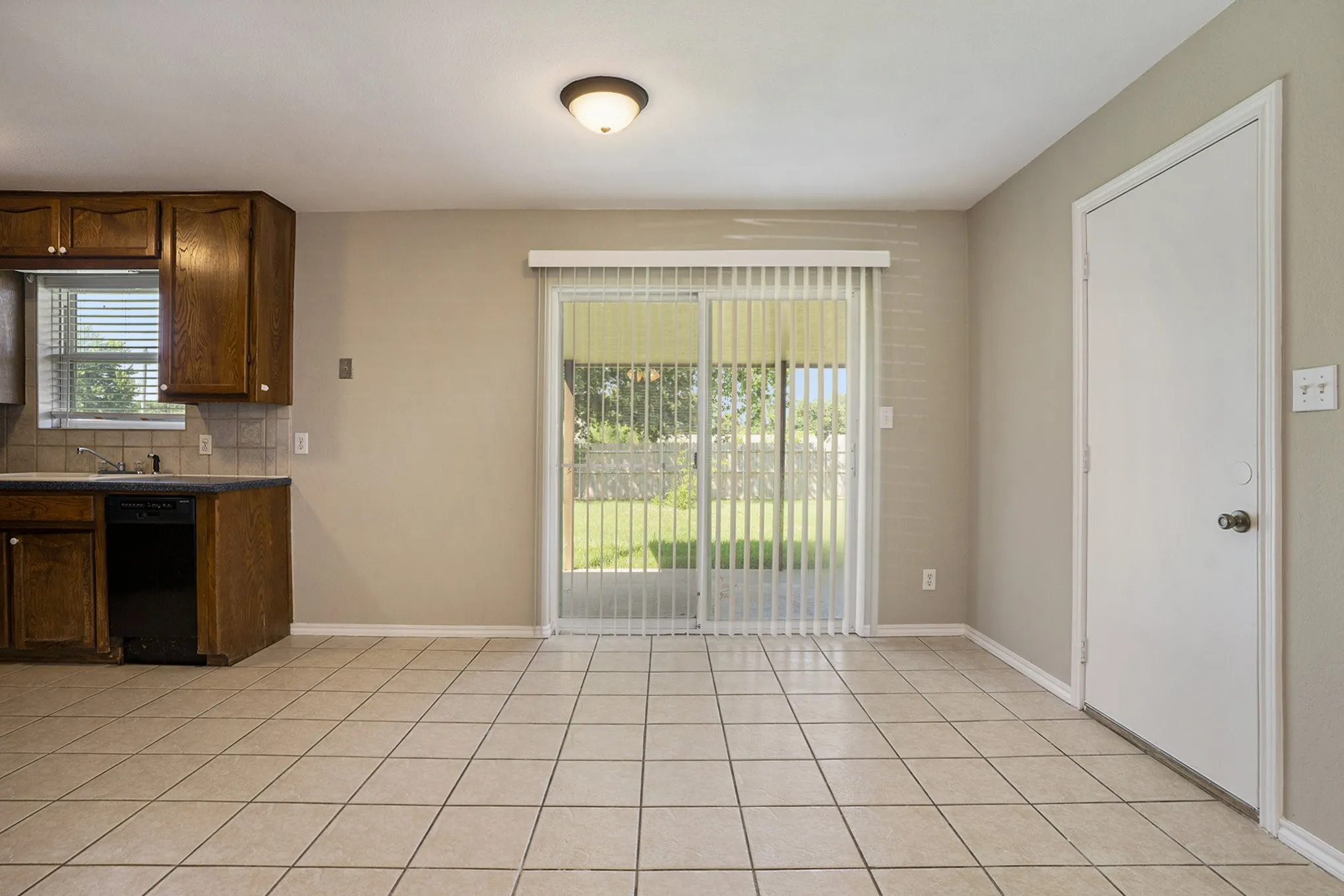 Tile flooring, wood cabinetry, sliding glass door with vertical blinds, recessed ceiling light fixture, and a built-in dishwasher