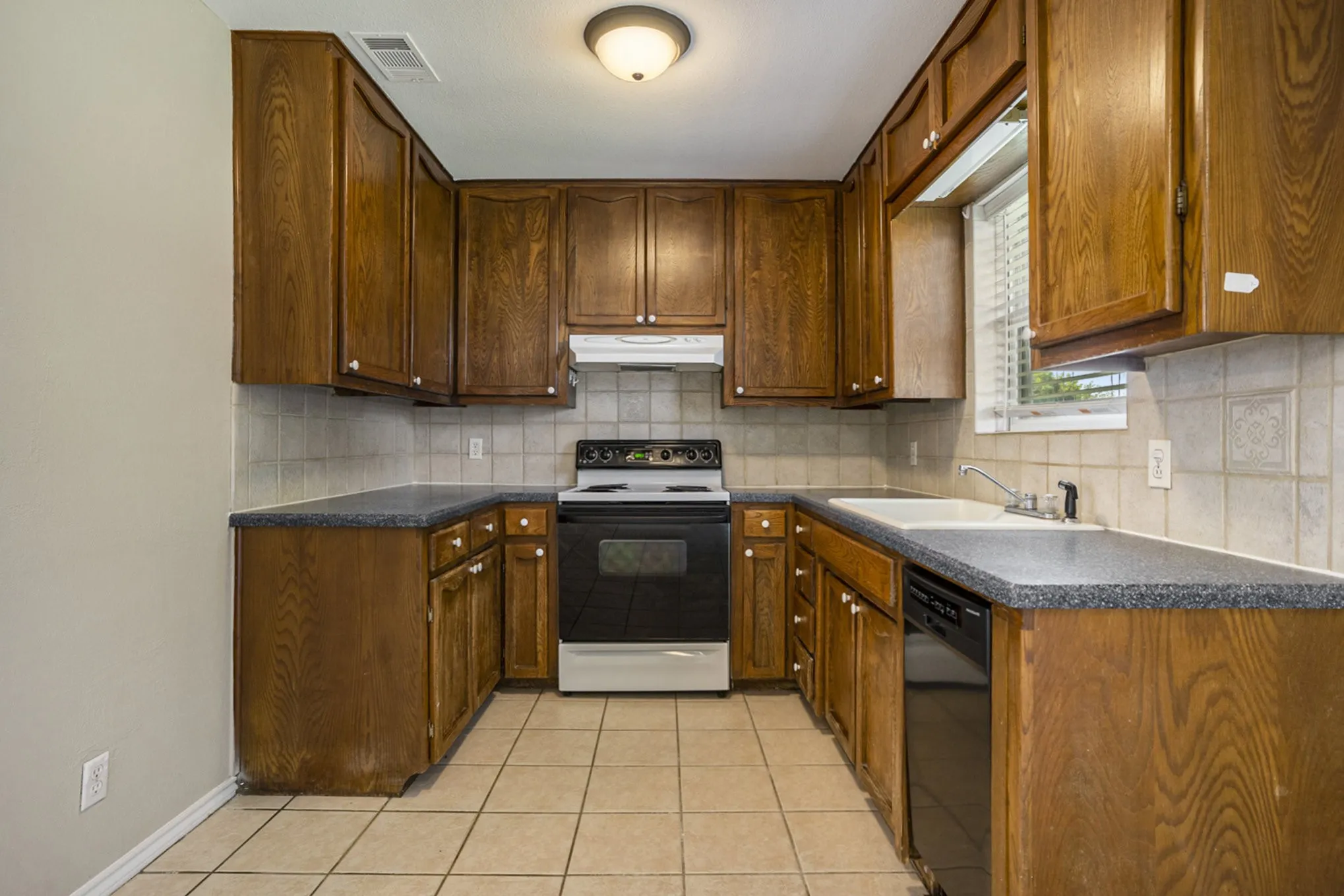 U-shaped kitchen featuring wood cabinetry, tile flooring, tile backsplash, and a double basin sink