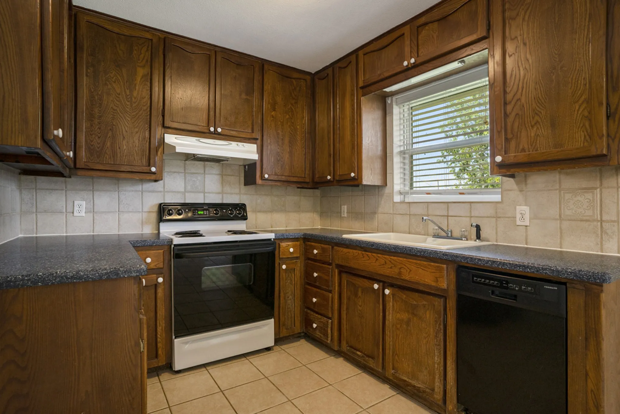 Kitchen featuring wood cabinetry, solid surface countertops, tile flooring, tile backsplash, and a window above the sink