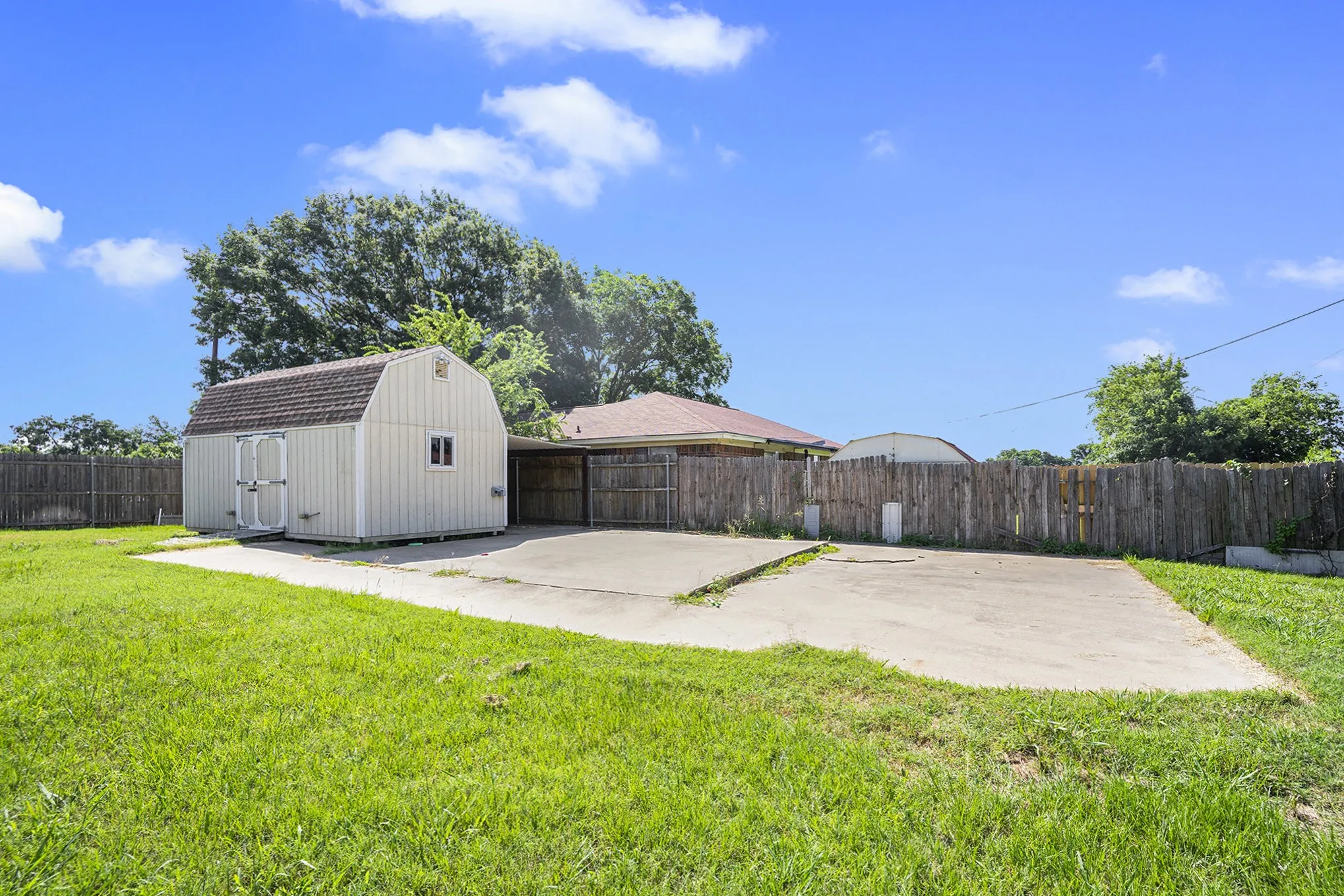 Expansive grassy yard featuring a storage shed with double doors, concrete patio, and wood privacy fencing