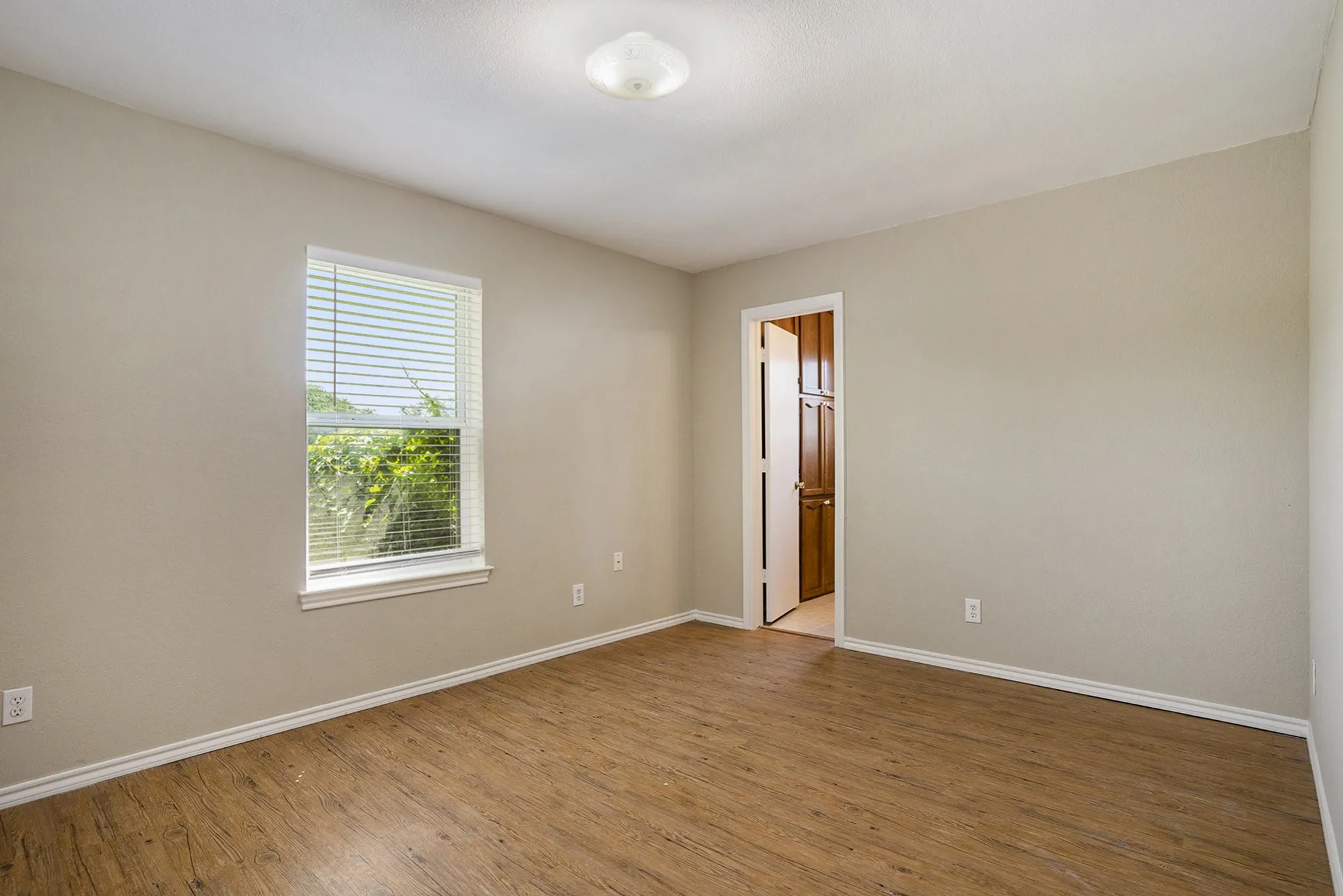 Wood-finish flooring with neutral wall tones and a window with blinds