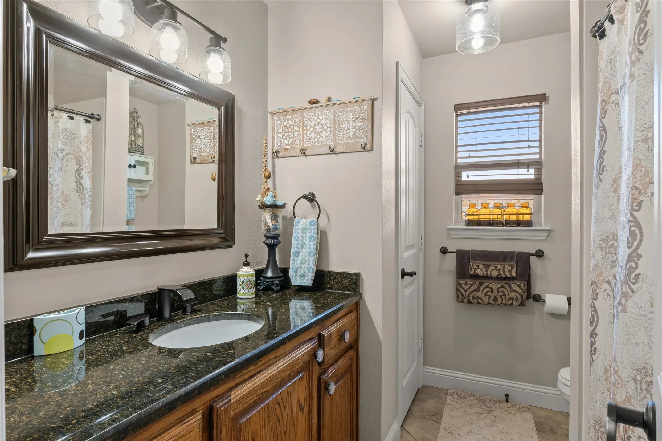 Vanity with dark countertop, undermount sink, dark-finish faucet, and wood-finish cabinetry