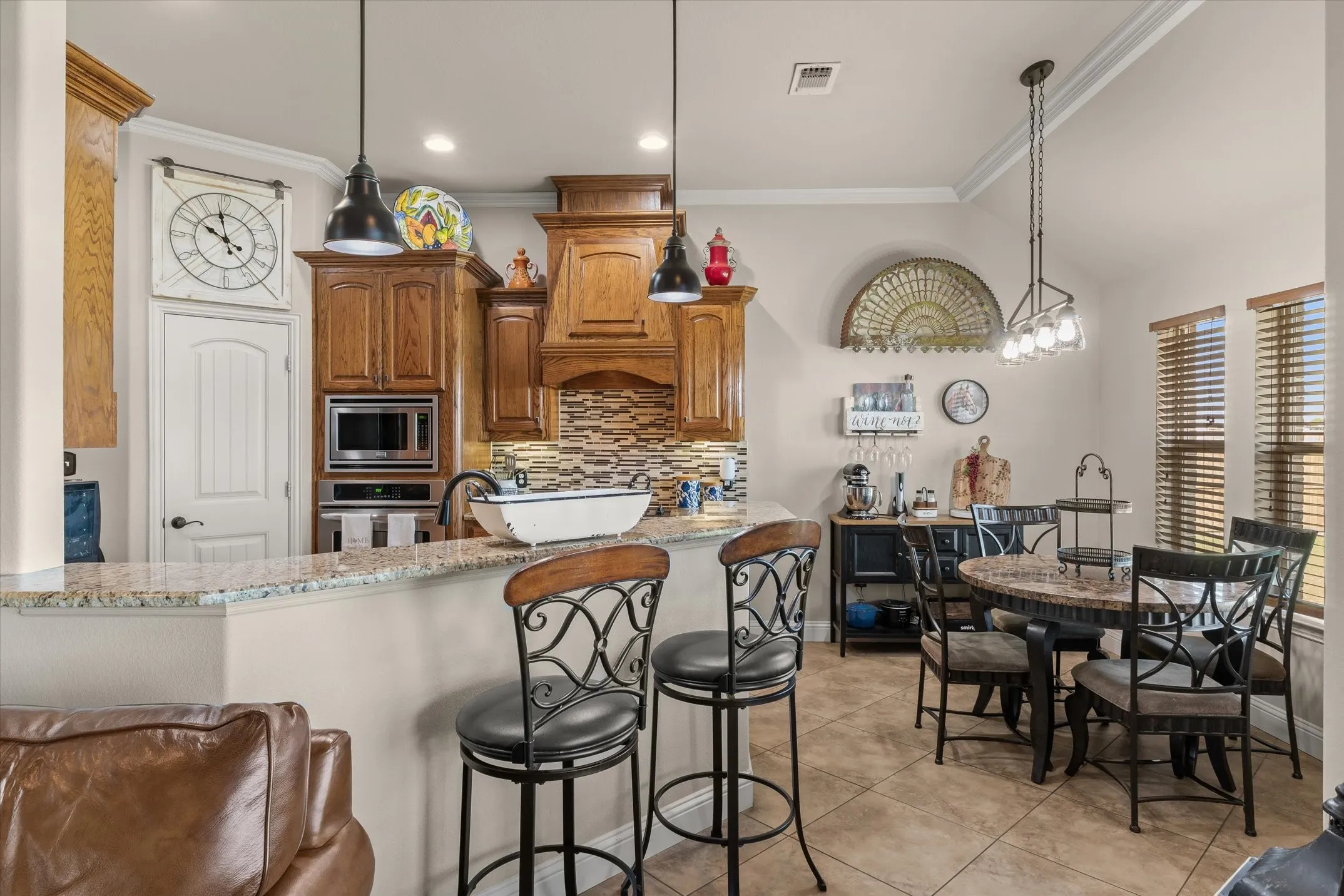 Kitchen featuring wood cabinetry, stainless steel appliances, a multi-tone backsplash, and a breakfast bar with stone countertops