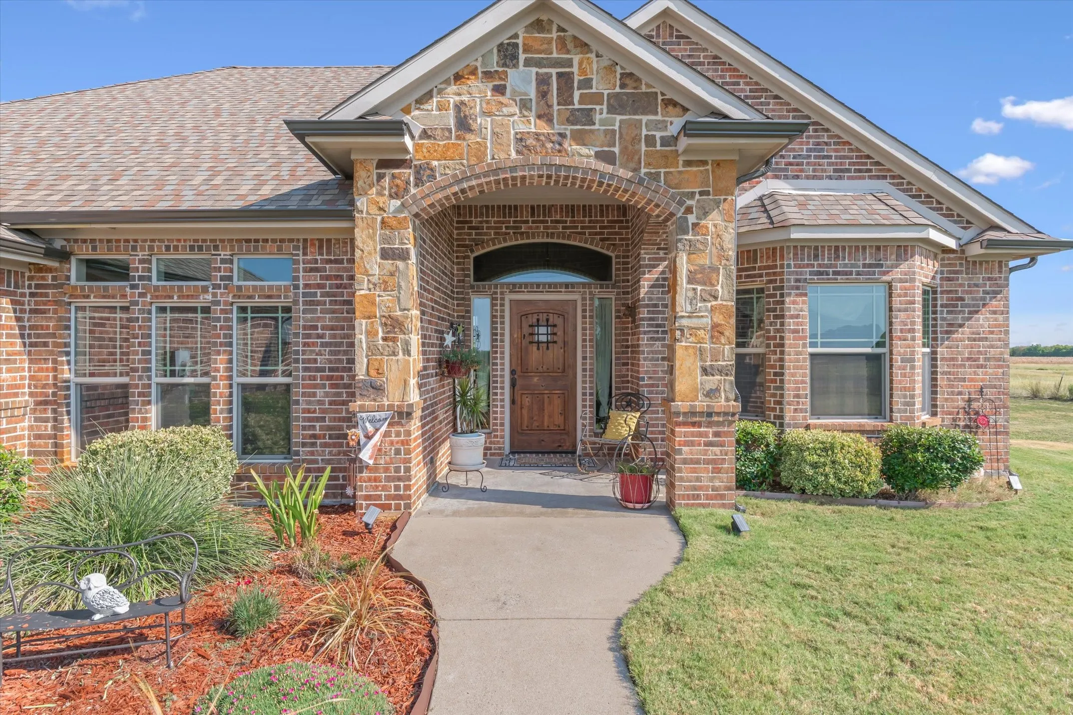 Brick exterior with stone accents, arched entryway, bay window, wood-finish front door, and concrete walkway