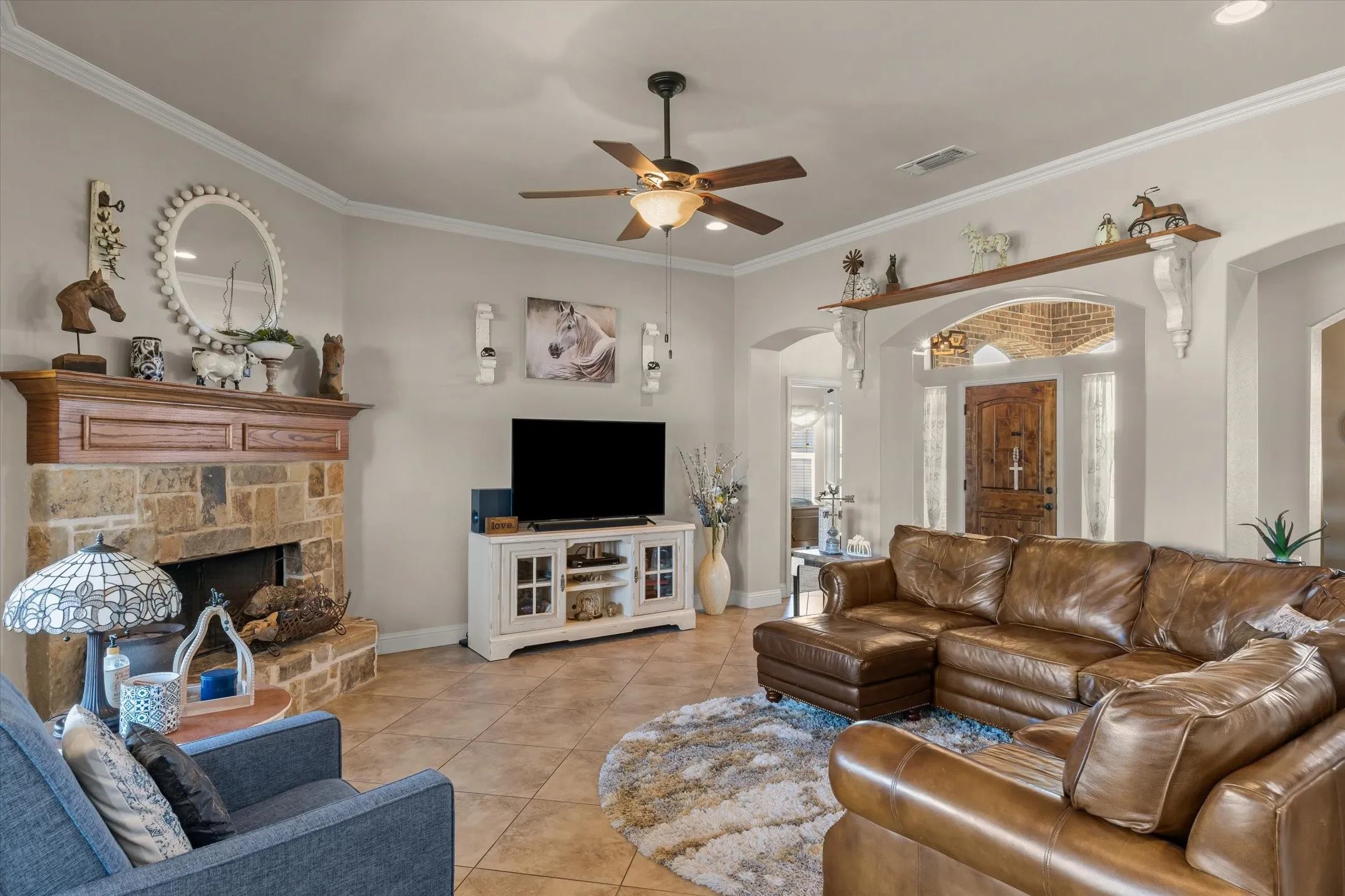 Stone-clad fireplace with a wood-mantel, tile flooring, crown molding, and an arched entry