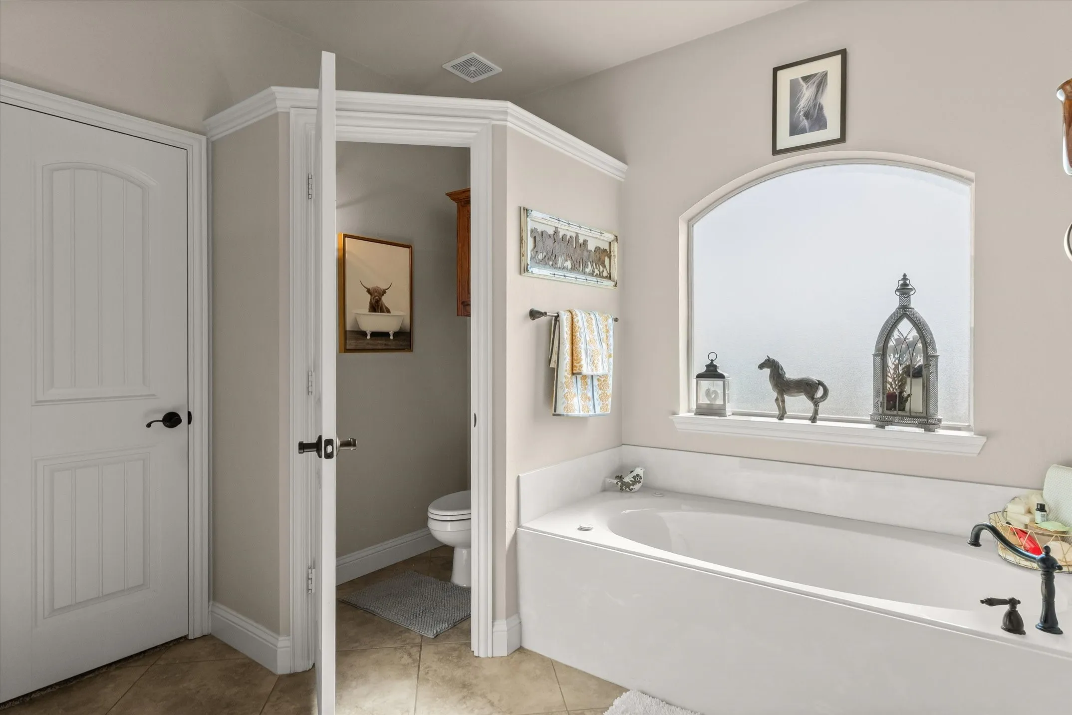 Built-in soaking tub with a dark bronze faucet, arched window, and tile flooring