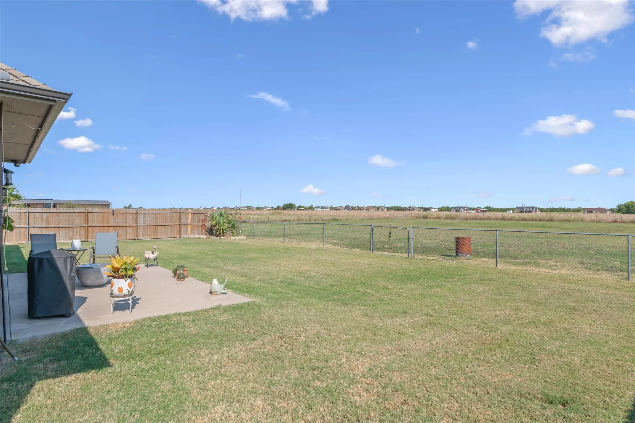 Expansive outdoor patio with a concrete slab, surrounded by a manicured lawn and a wood privacy fence