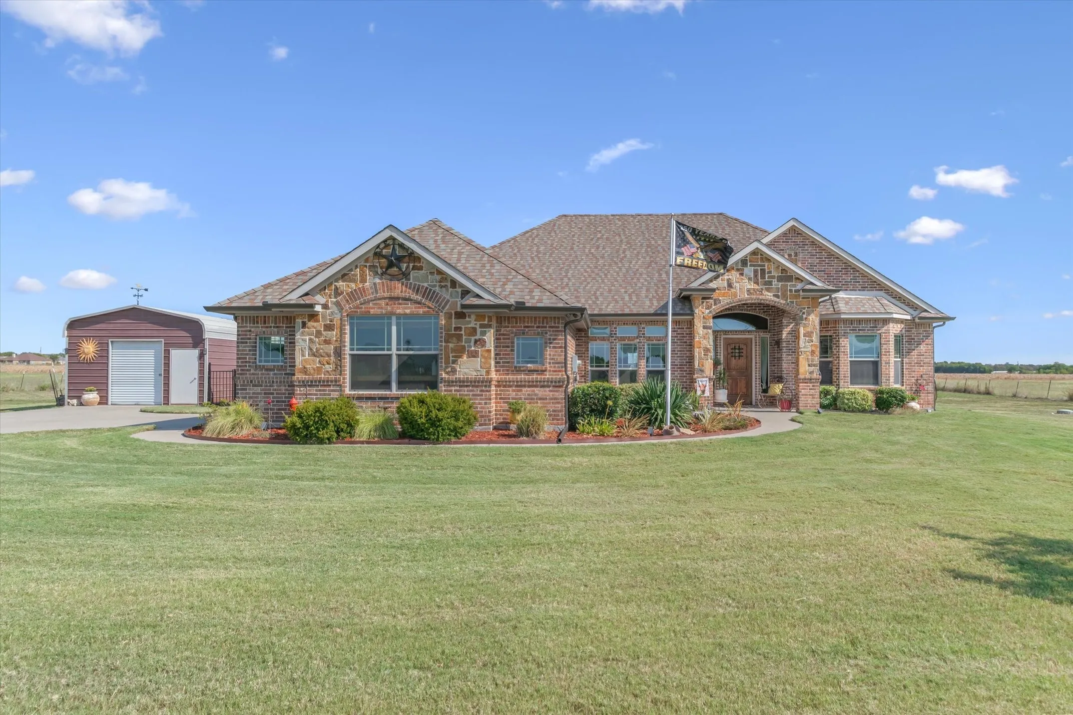 Brick and stone exterior with an arched entryway, mature landscaping, and an expansive lawn