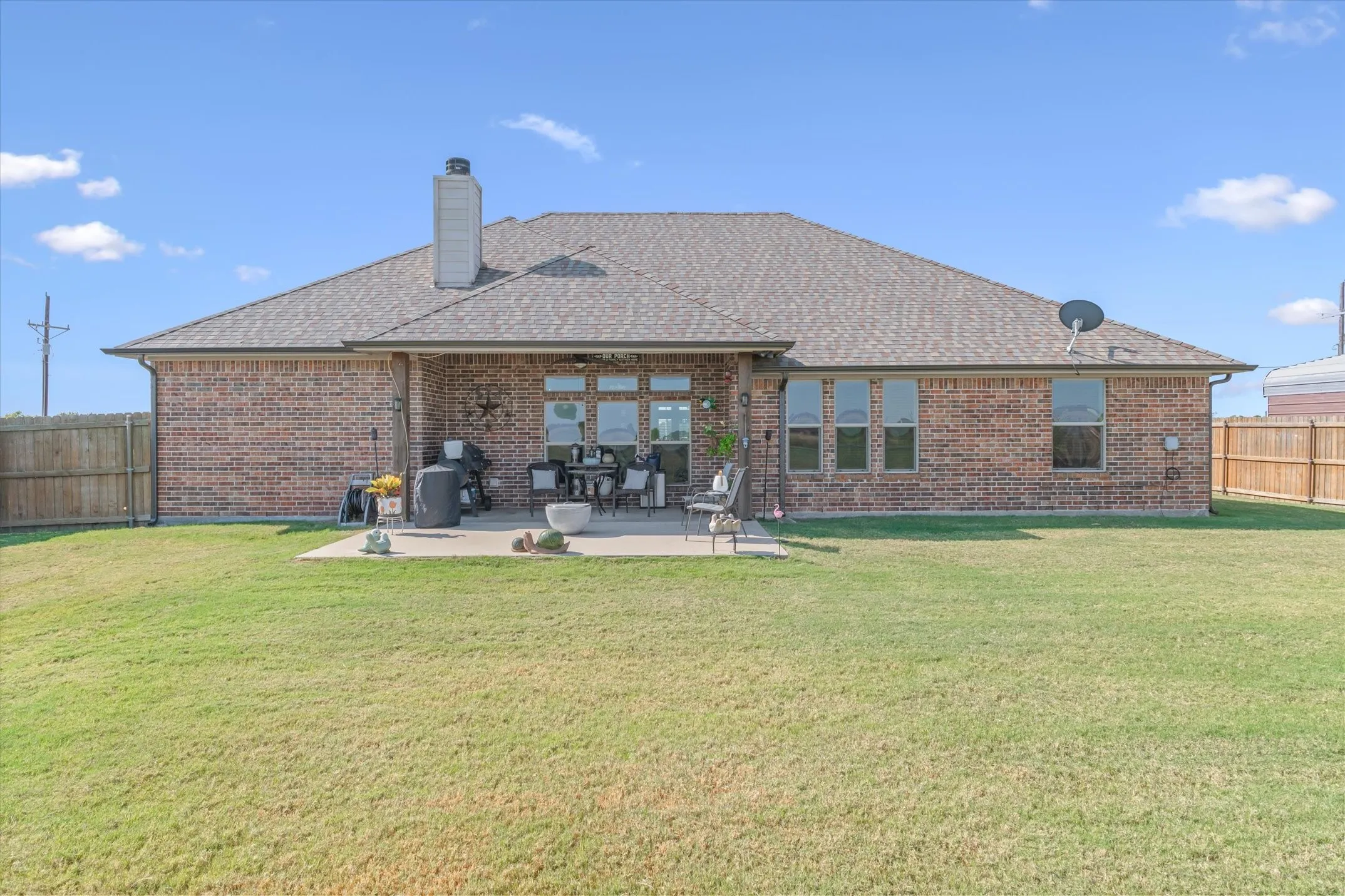 Brick exterior with a gabled shingle roof, featuring a chimney and an extended patio
