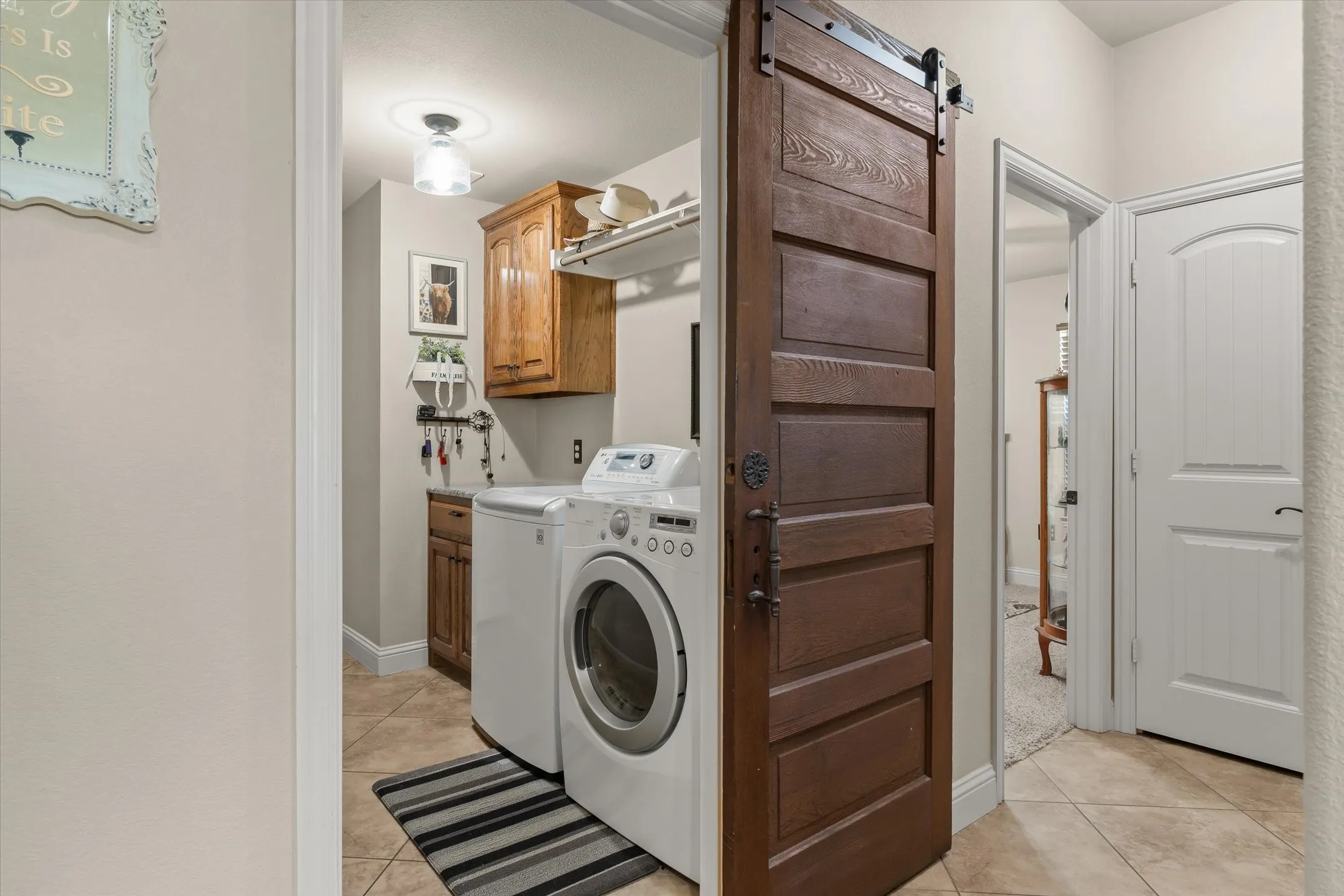 Laundry area featuring a dark wood-finish barn door, tile flooring, wood cabinetry, and a ceiling-mounted light fixture